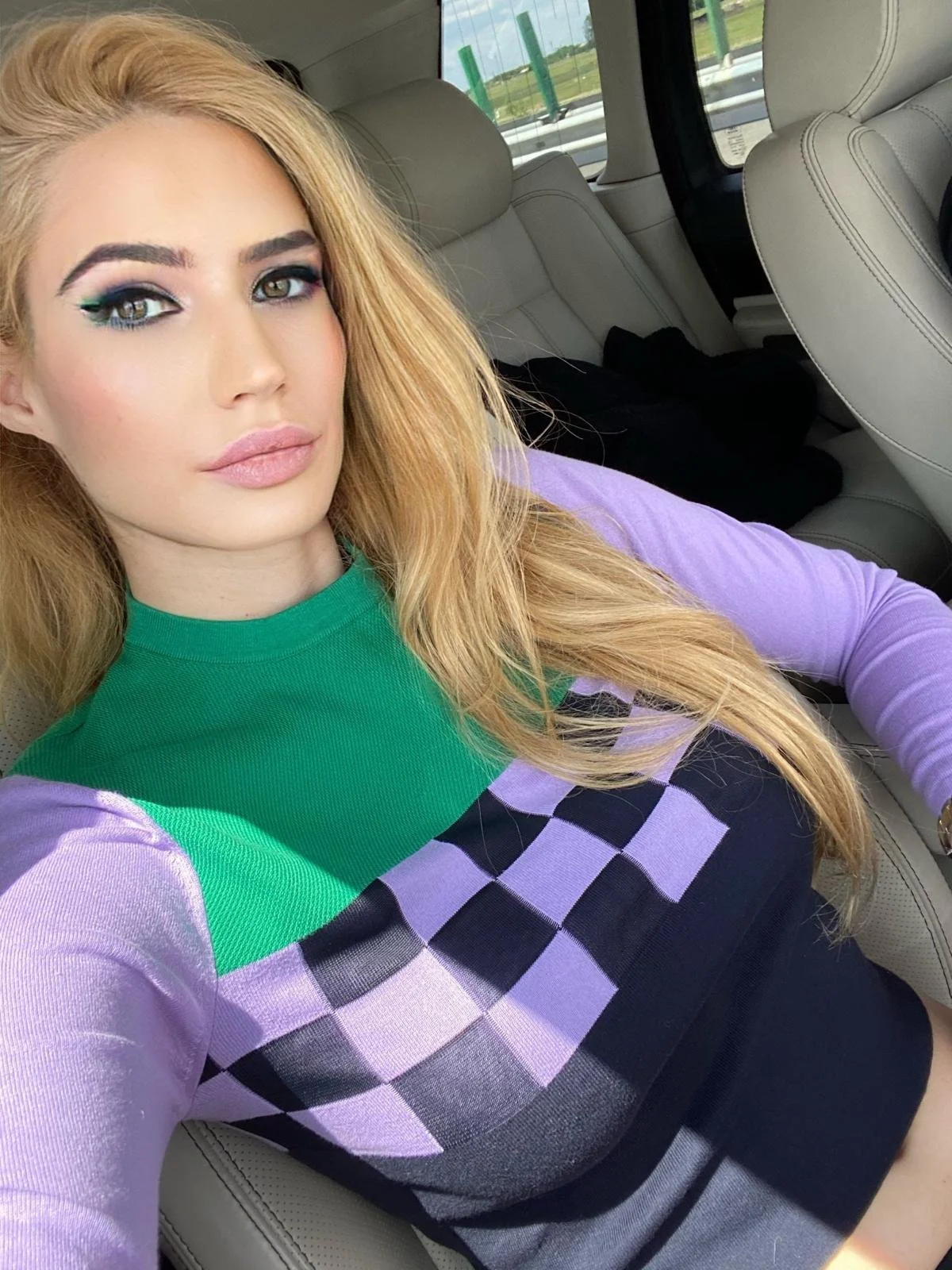 Sienna Blakely, a beautiful blonde independent escort and luxury London companion, taking a close-up selfie in a colourful green, purple and black outfit.