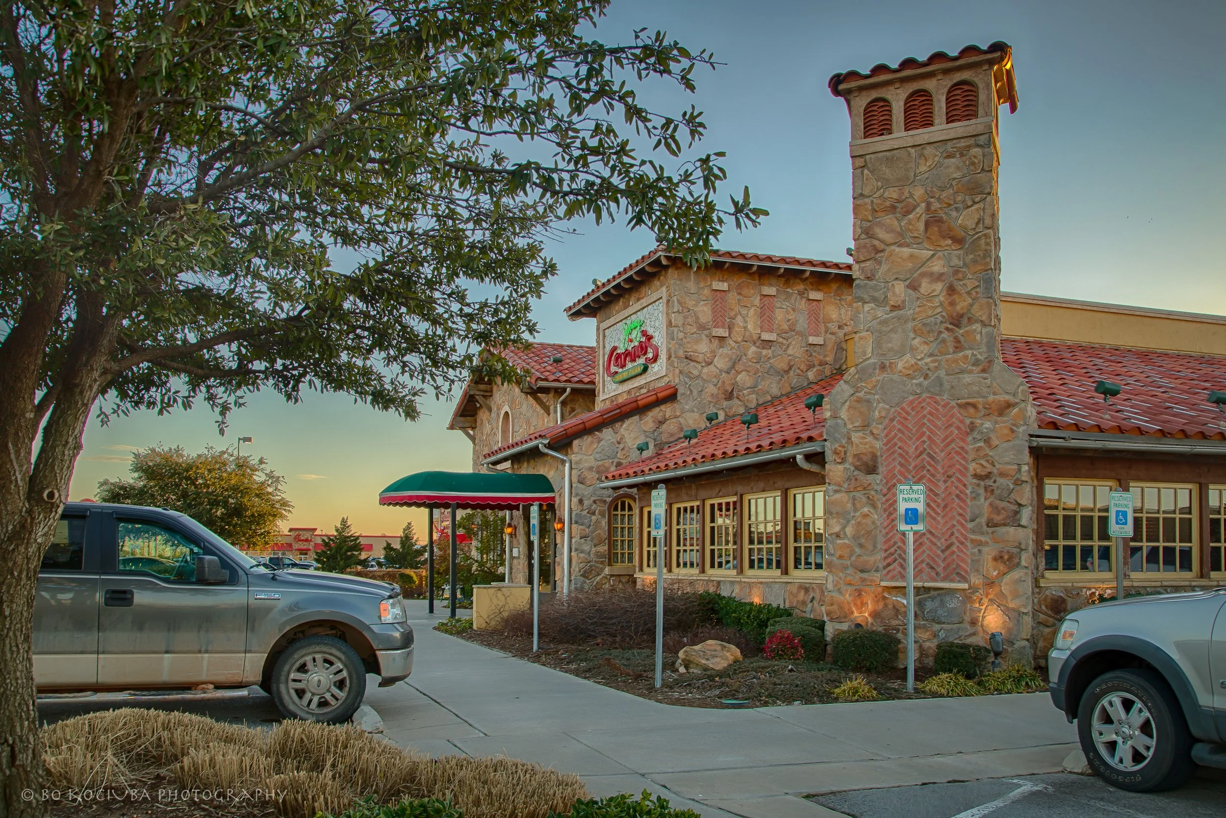 Johhny Carino's restaurant stone commercial building along Garth Brooks Boulevard in Yukon, Oklahoma, featuring a red tile roof, prominent chimney, and landscaped surroundings.