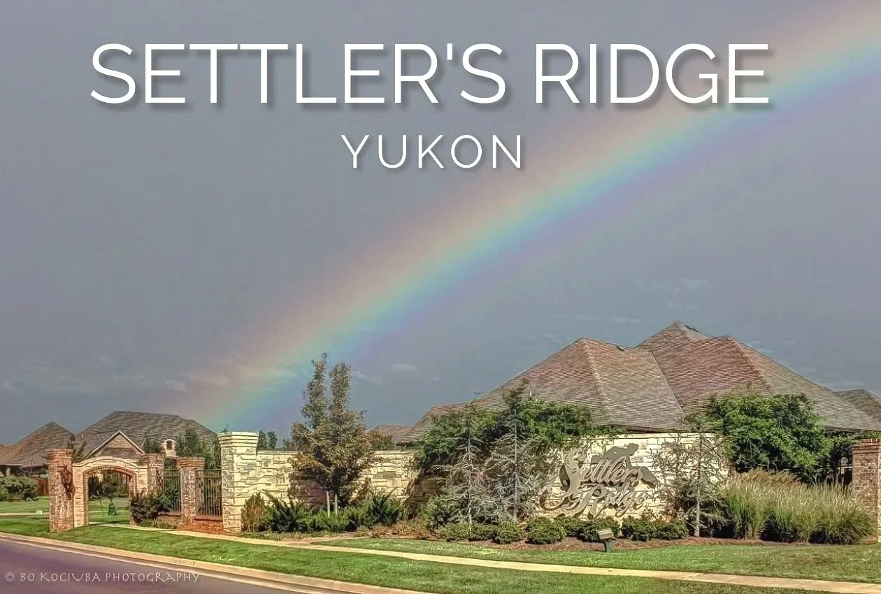 Settlers Ridge neighborhood entrance in Yukon, Oklahoma, with landscaped grounds, residential homes, and a rainbow overhead.