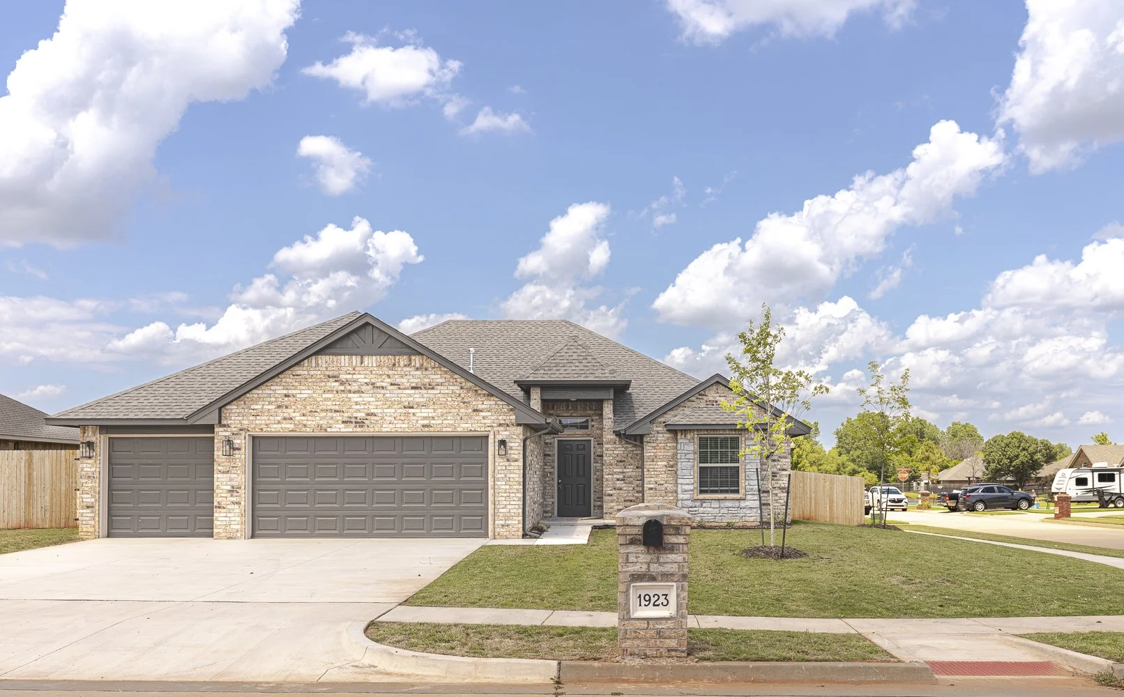Brick and stone home at 1923 W Flintlock Way in Hunters Hill, Mustang, Oklahoma, featuring an attached three-car garage, landscaped front yard, and brick mailbox.