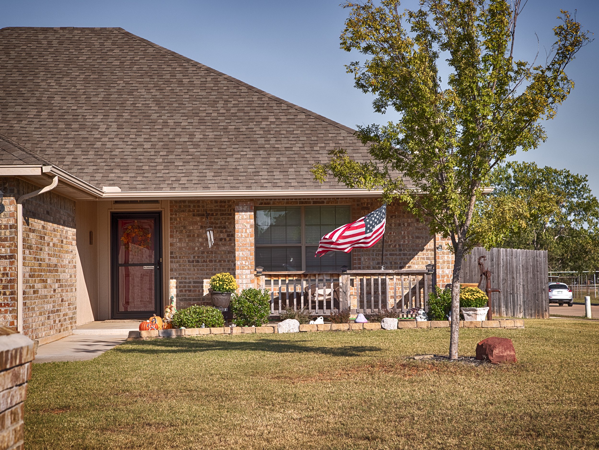 Brick home in Hunters Hill, Mustang, Oklahoma, with a covered front porch decorated with pumpkins, potted plants, and an American flag.