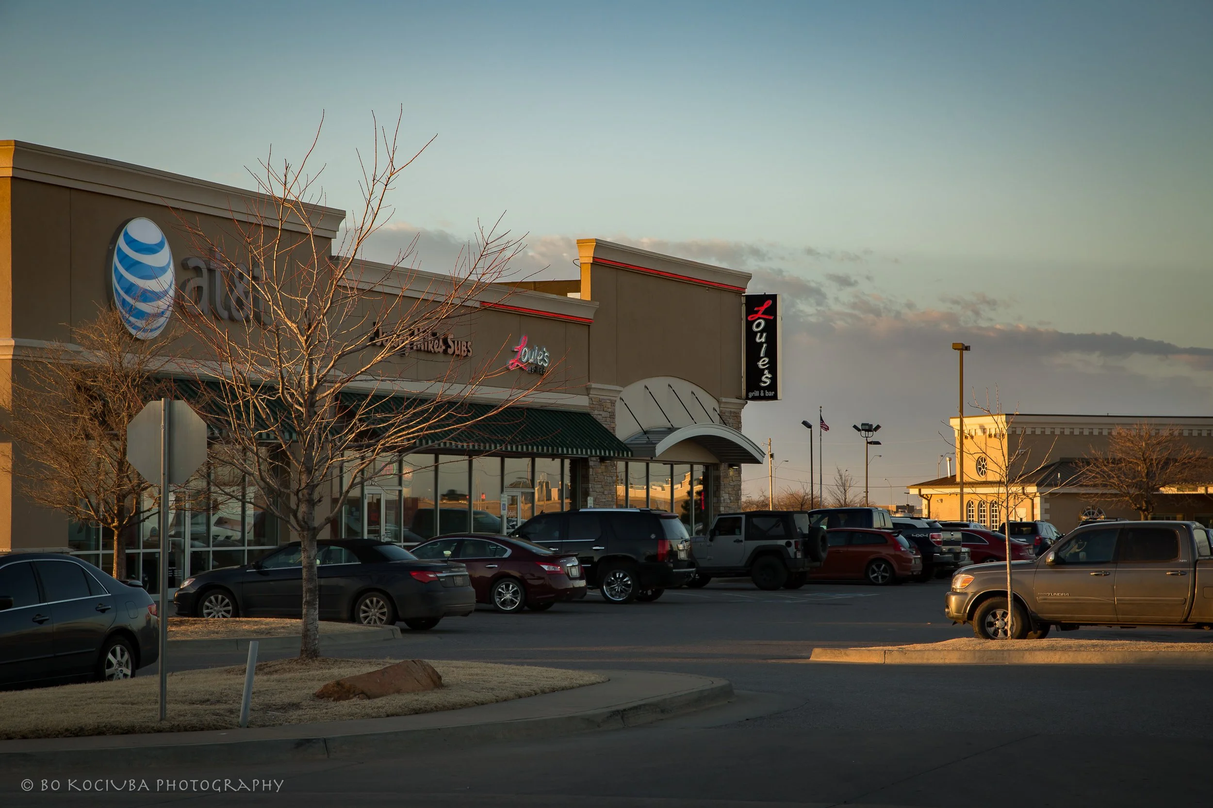 Louie's Grill & Bar in Yukon, Oklahoma, photographed in the evening with storefronts, outdoor lighting, and cars parked along the shopping center.