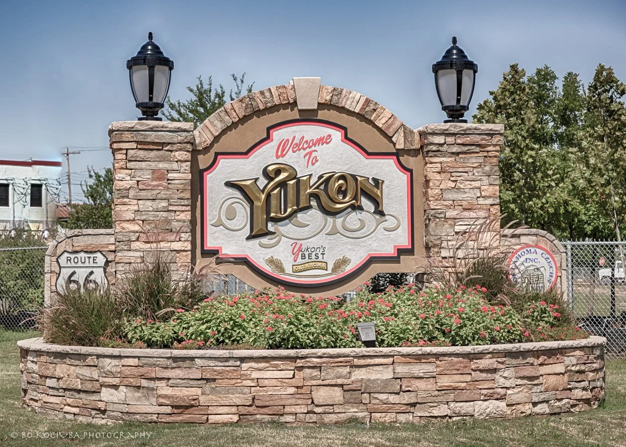 Welcome to Yukon, Oklahoma, monument along historic Route 66, featuring stonework, decorative landscaping, and traditional lanterns.