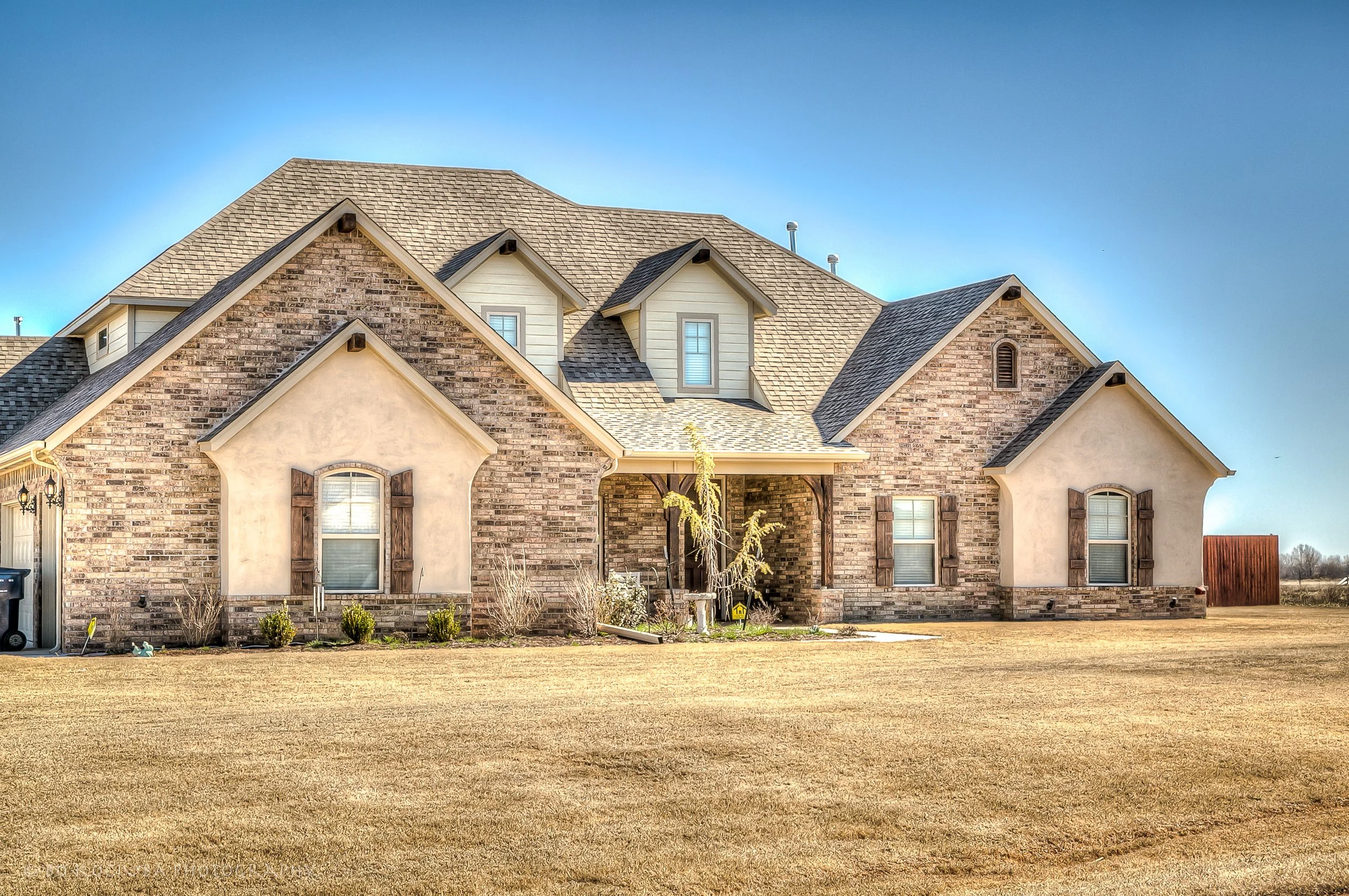 Two-story brick and stone home in Chisholm Run, Yukon, Oklahoma, with prominent gabled rooflines, arched front entry, and a spacious front lawn.