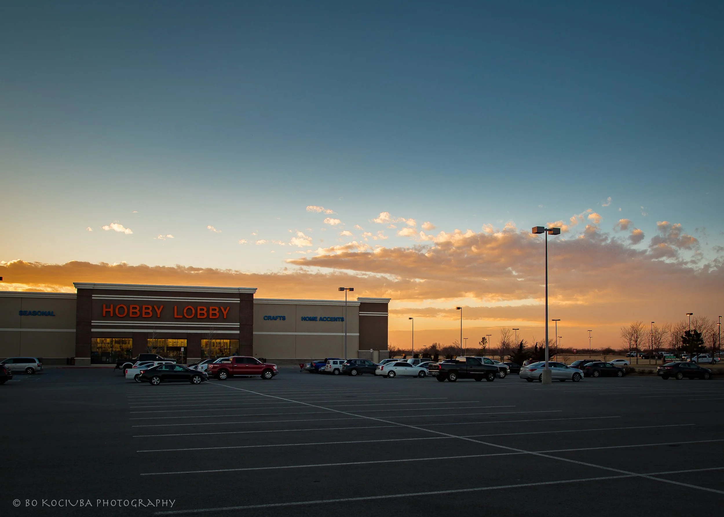 Hobby Lobby store along Garth Brooks Boulevard in Yukon, Oklahoma, with its parking area and a colorful sunset sky.