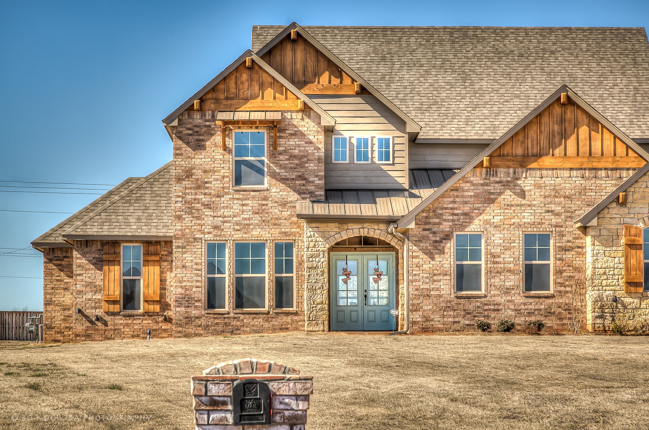 Brick home in Chisholm Run, Yukon, Oklahoma, featuring multiple steep gables, large front windows, and double entry doors with decorative glass.
