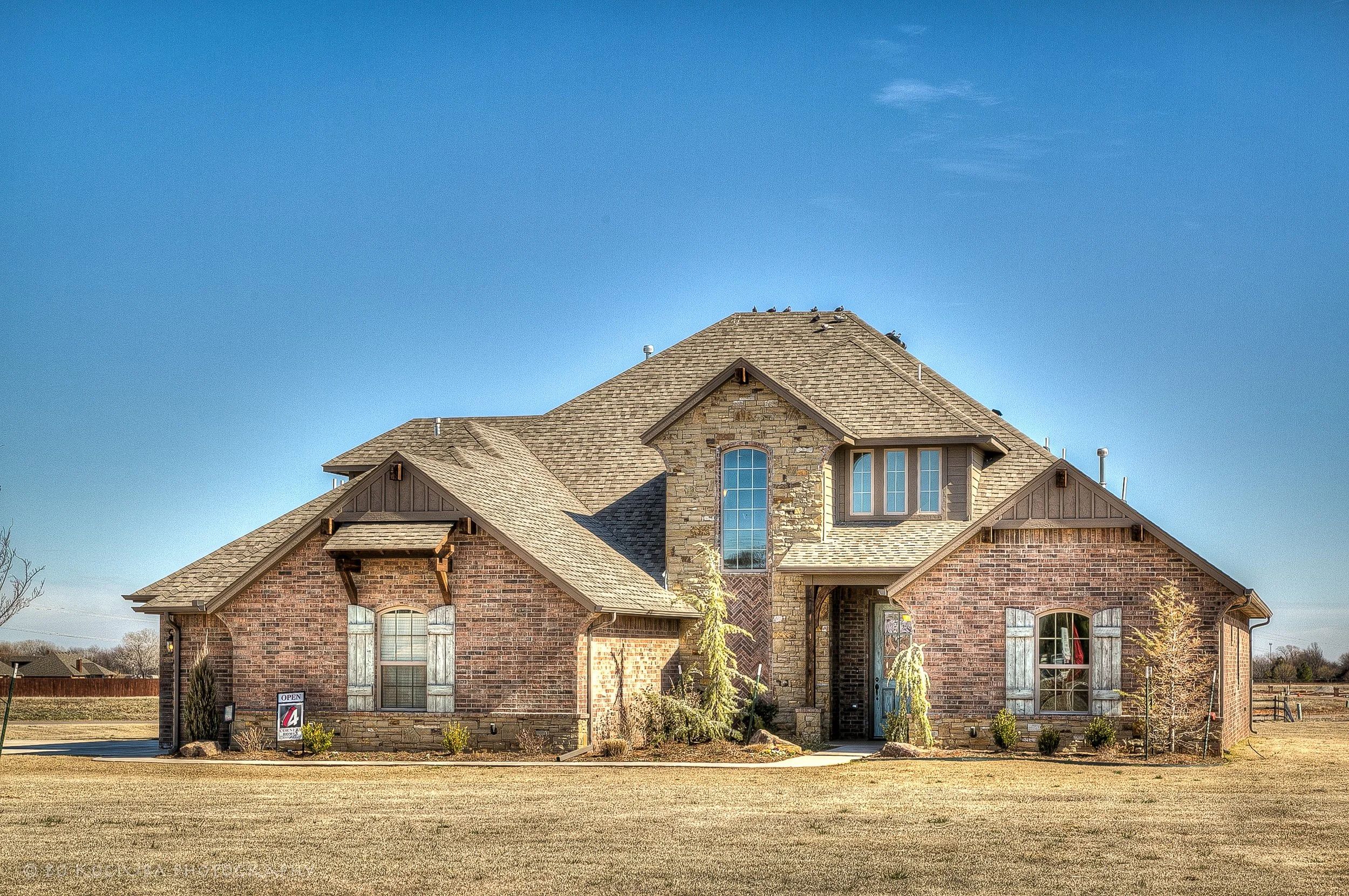 Two-story brick and stone home in Chisholm Run, Yukon, Oklahoma, featuring steep gabled rooflines, arched windows, and a front lawn.