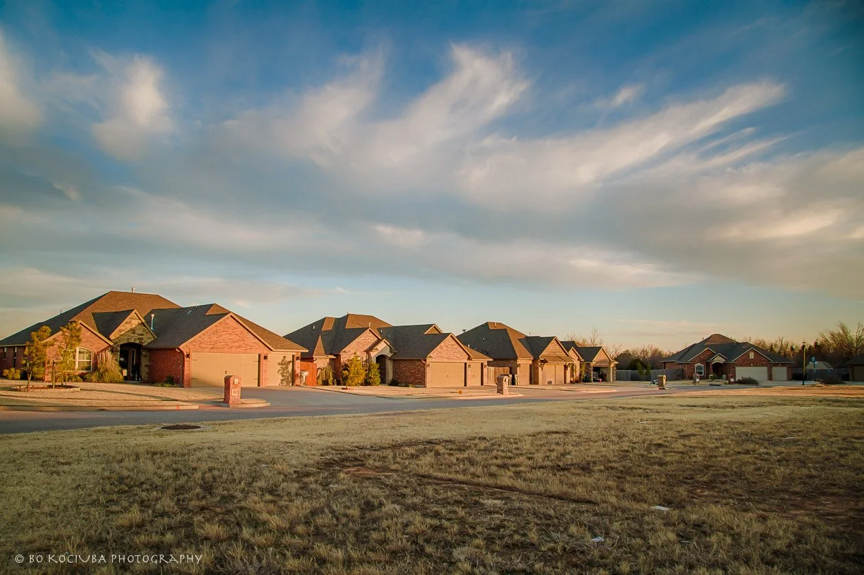 Row of brick homes with attached garages in Sabram Estates, Yukon, Oklahoma, photographed in warm evening light beneath a partly cloudy sky.