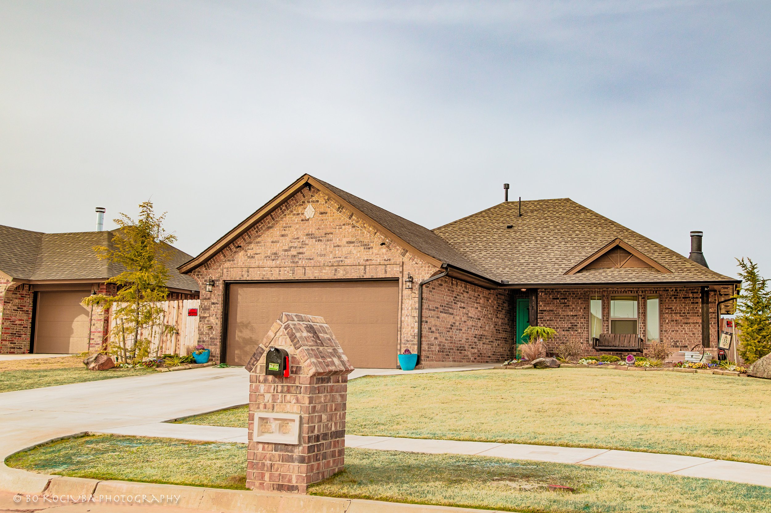 Red brick home in Chisholm Crossing, Yukon, Oklahoma, featuring multiple gabled rooflines, a covered front entry, attached garage, and landscaped shrubs.