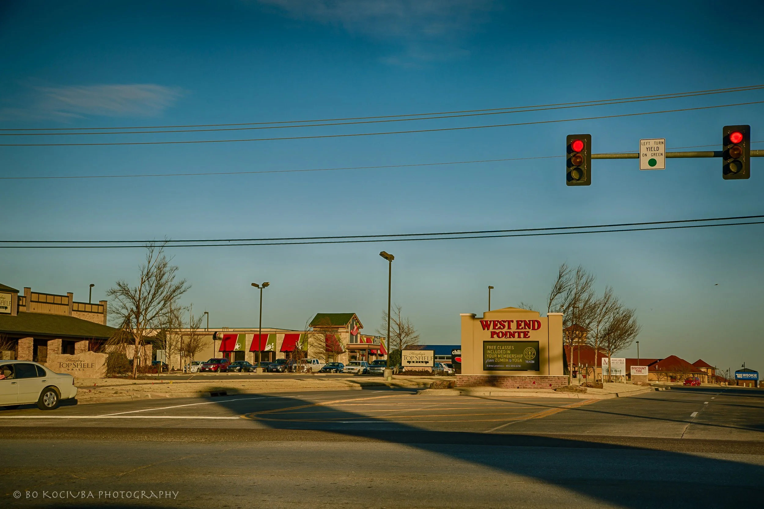 Shopping centers along Garth Brooks Boulevard in Yukon, Oklahoma, with retail storefronts, parking areas, and a signalized intersection.