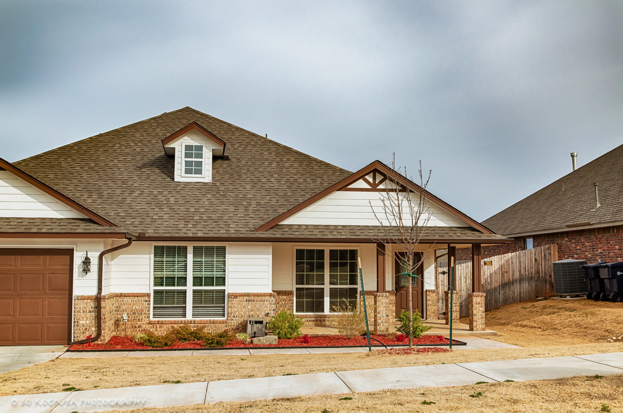 Single-story home in Chisholm Crossing, Yukon, Oklahoma, with white siding, brick accents, an attached two-car garage, and a landscaped front lawn.