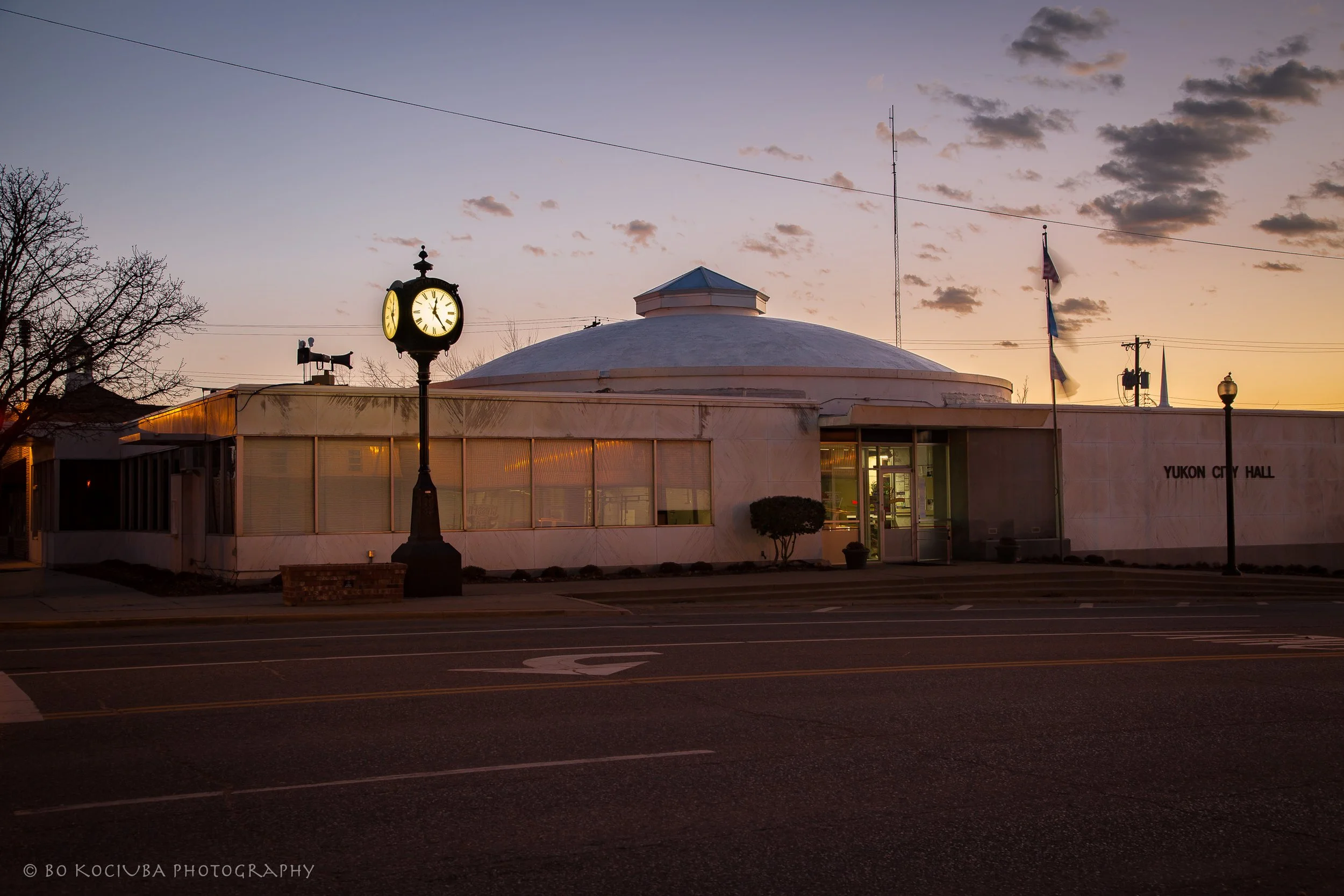 Yukon City Hall along historic Route 66 in downtown Yukon, Oklahoma, with its clock tower, flags, and evening sky.