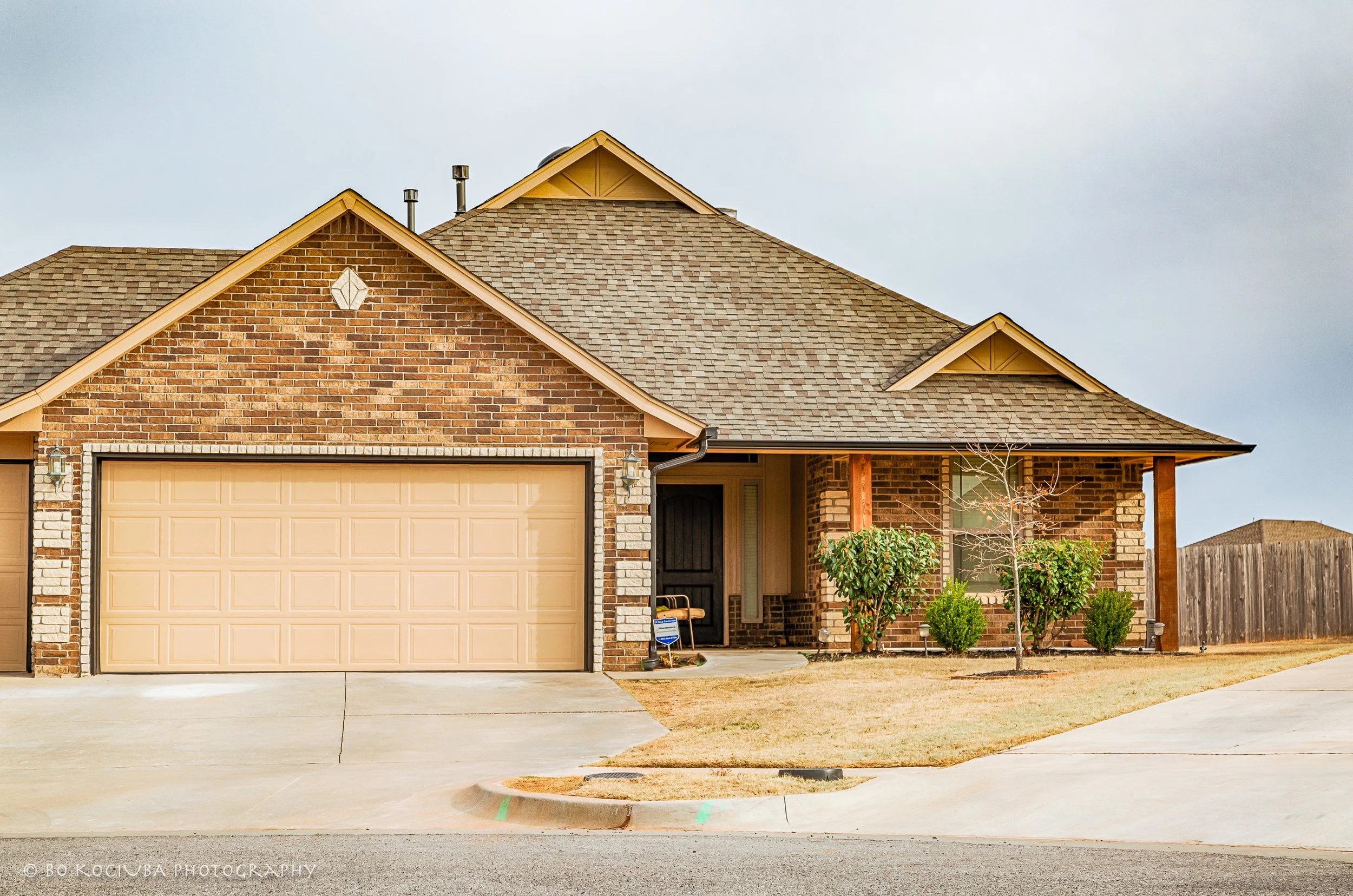 Single-story brick home in Chisholm Crossing, Yukon, Oklahoma, with an attached two-car garage, covered front porch, and landscaped planting beds.