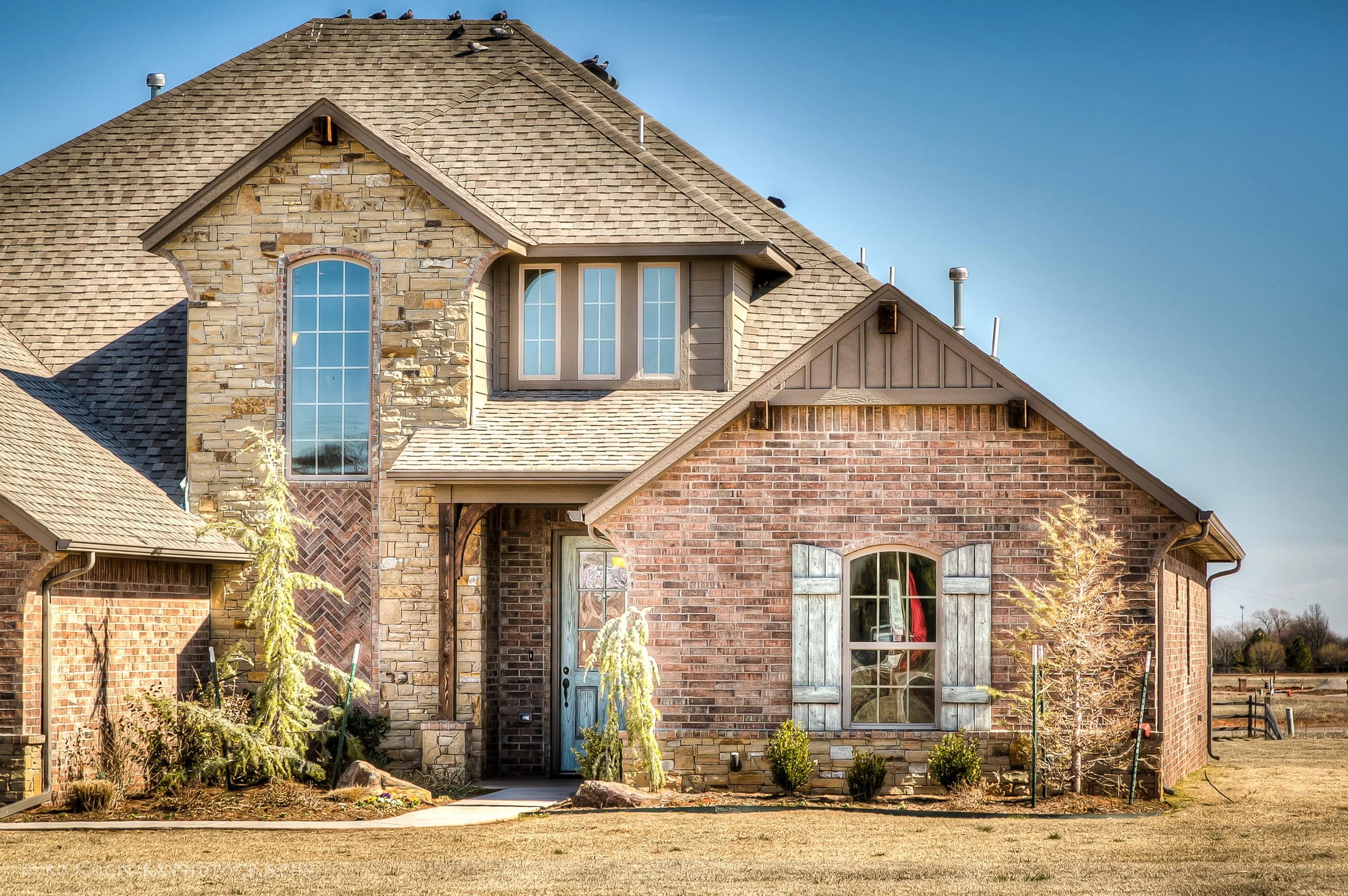 Close-up of a two-story brick and stone home in Chisholm Run, Yukon, Oklahoma, showing its prominent gables, large windows, and architectural stonework.