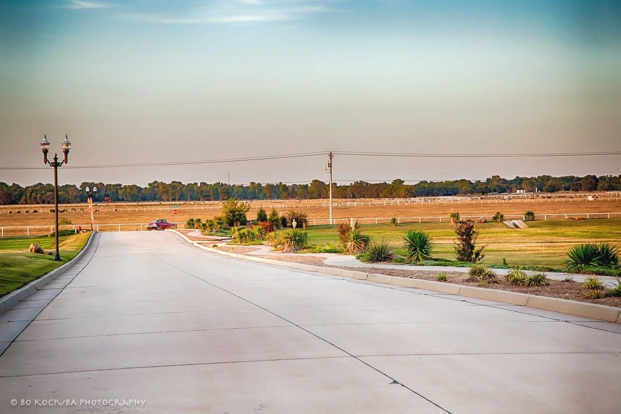 Landscaped entrance drive with decorative lighting, planted beds, and open views across the surrounding Oklahoma countryside.