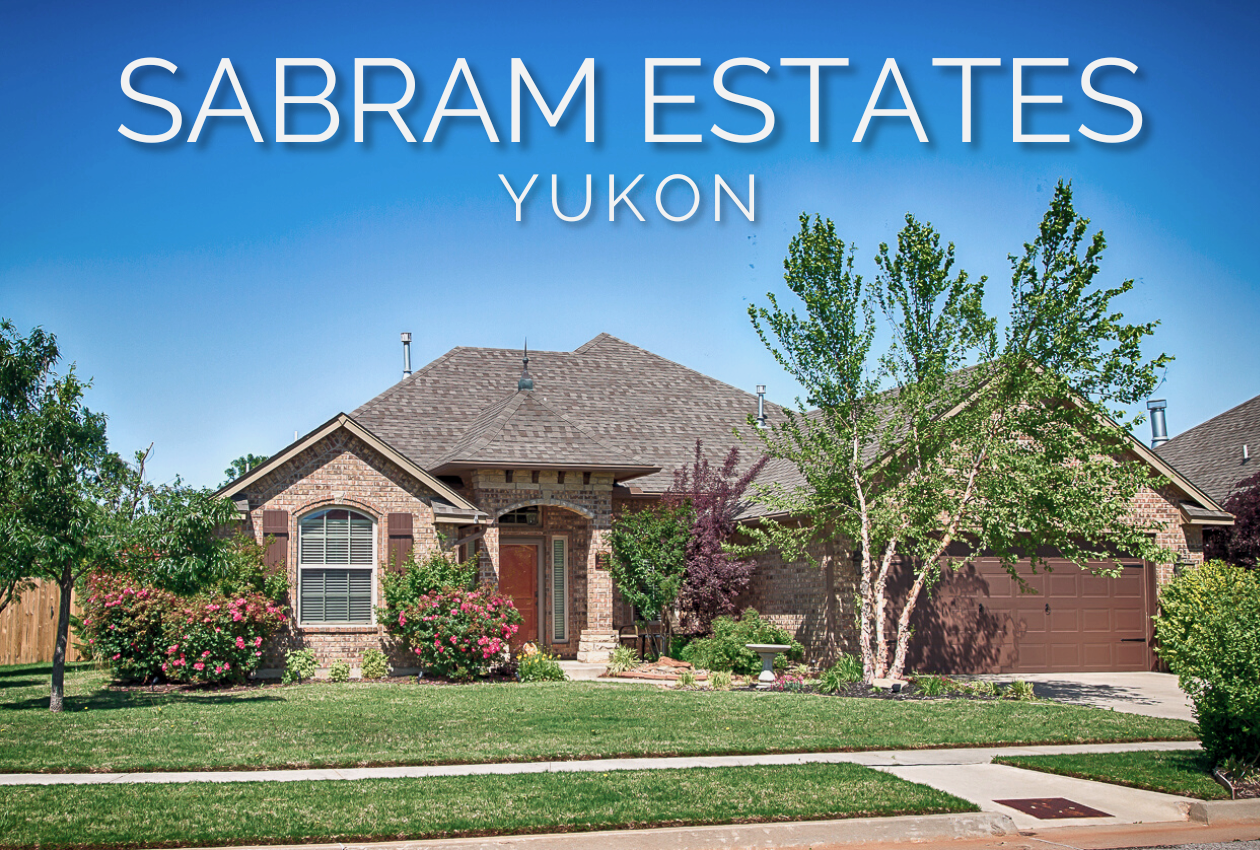 Brick home in Sabram Estates near Lake Overholser in Yukon, Oklahoma, with a landscaped front lawn, mature trees, and flowering shrubs.
