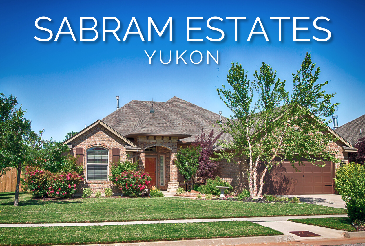 Brick home in Sabram Estates, Yukon, Oklahoma, featuring a landscaped front yard, mature trees, flowering shrubs, and a covered entry.