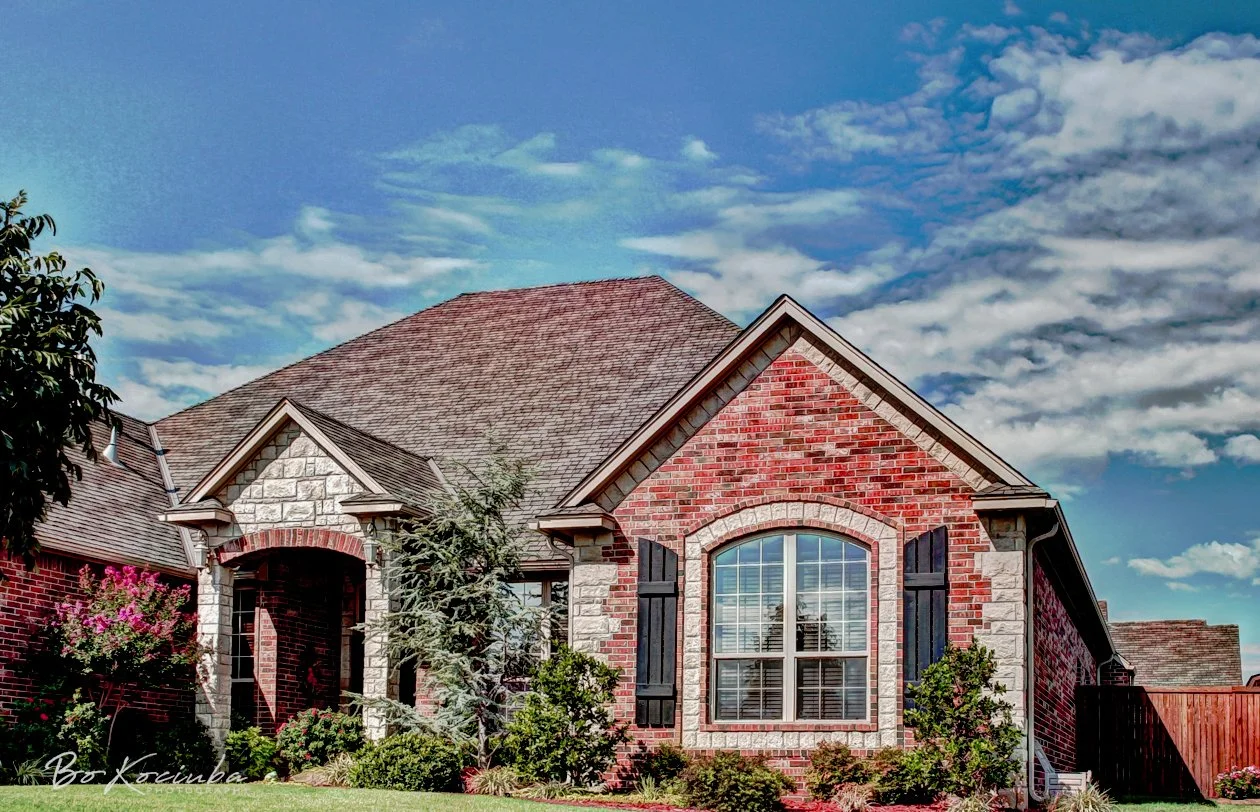 Brick home in Settlers Ridge, Yukon, Oklahoma, with prominent gabled rooflines, an arched front window, and landscaped flower beds.