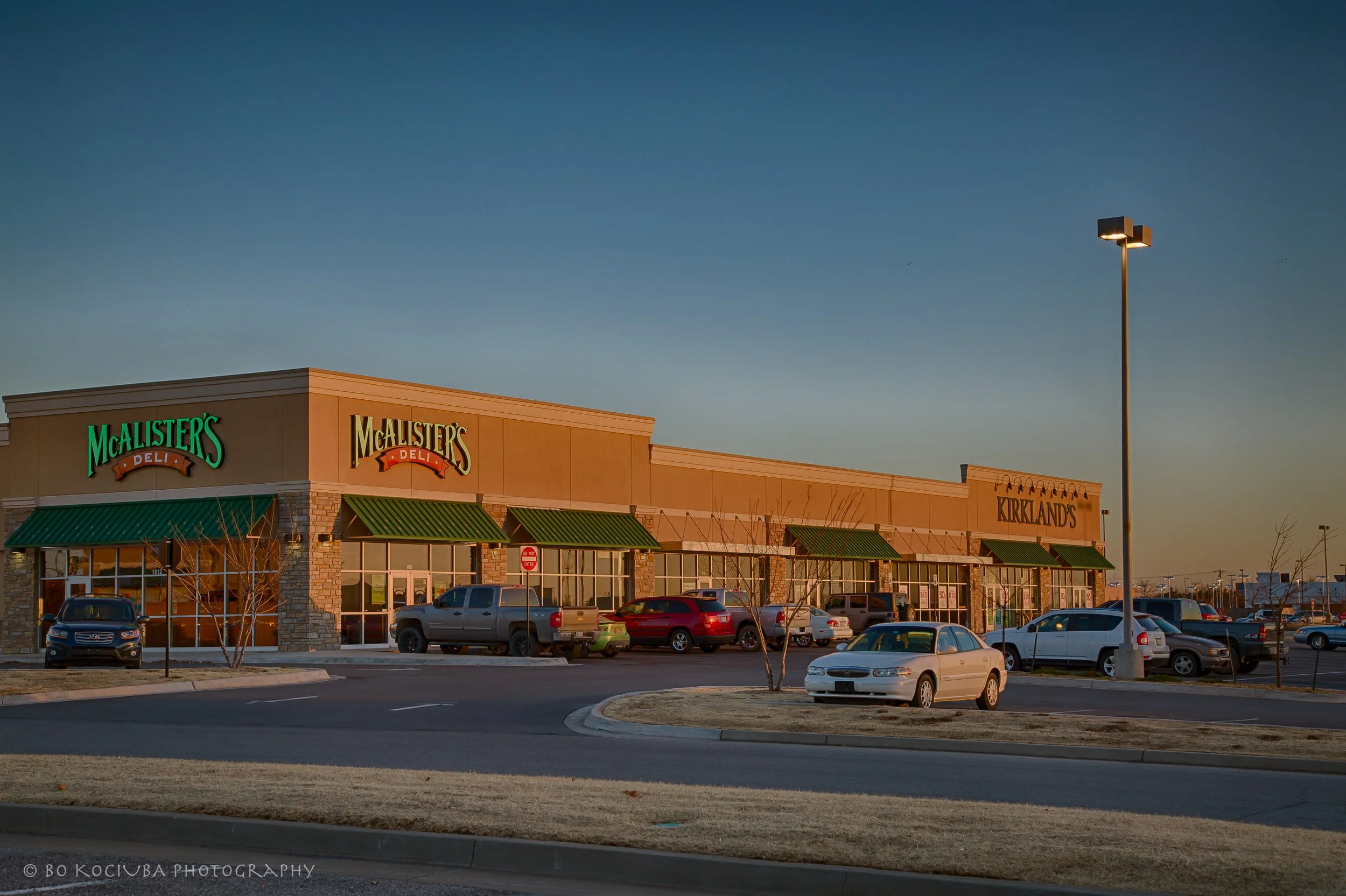 Shopping center on Garth Brooks Boulevard in Yukon, Oklahoma, featuring McAlister's Deli and Kirkland's storefronts in the evening light.