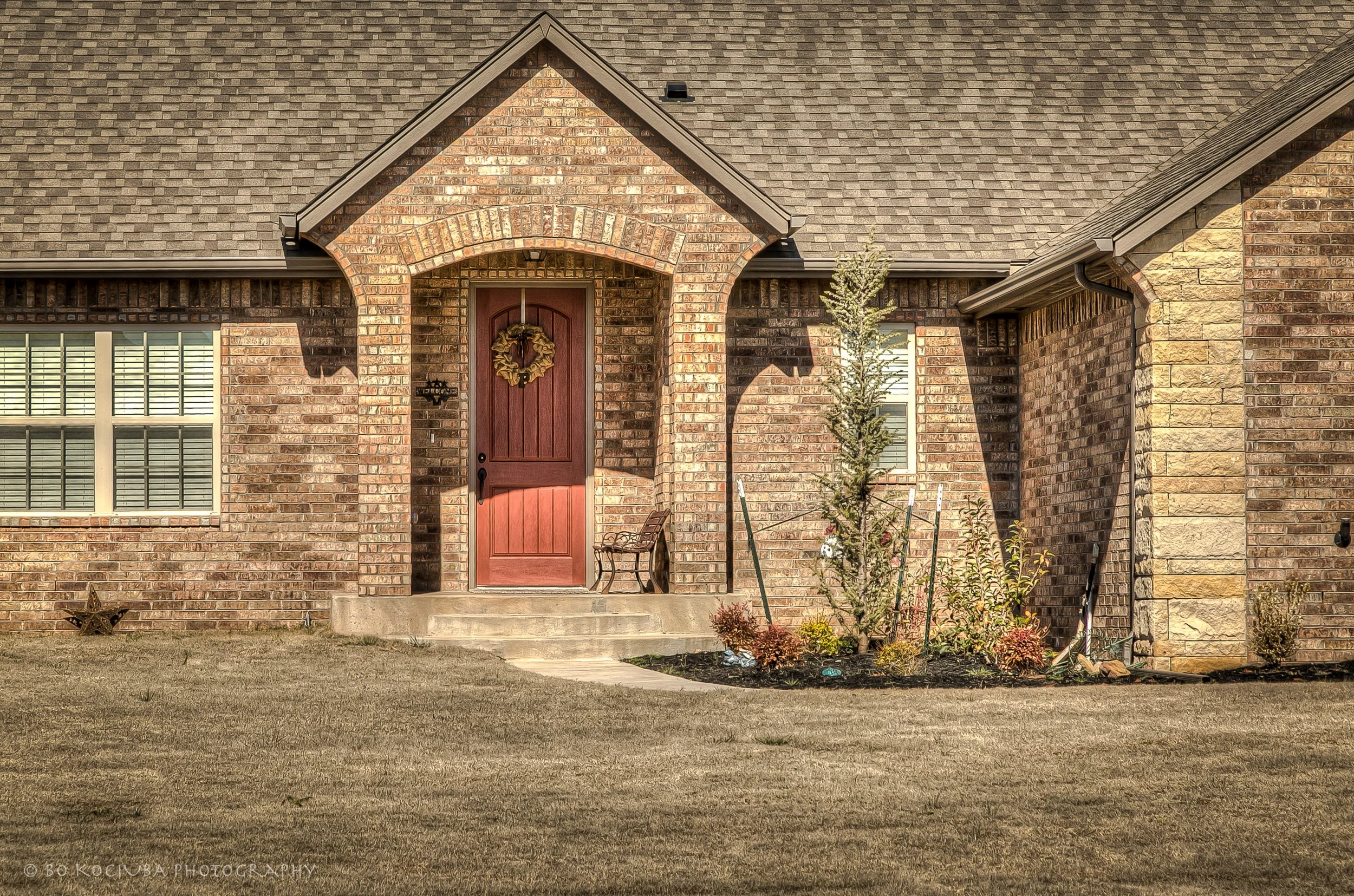 Brick home in Chisholm Run, Yukon, Oklahoma, featuring a red front door with a decorative wreath, arched entry, and landscaped front yard.