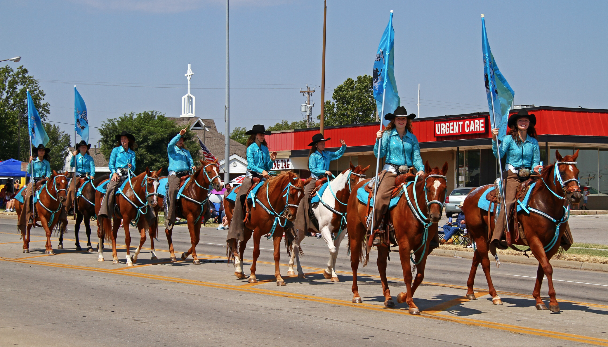 Women riding horses in formation during Mustang Western Days parade in Mustang, Oklahoma, wearing matching blue shirts and cowboy hats while carrying flags.