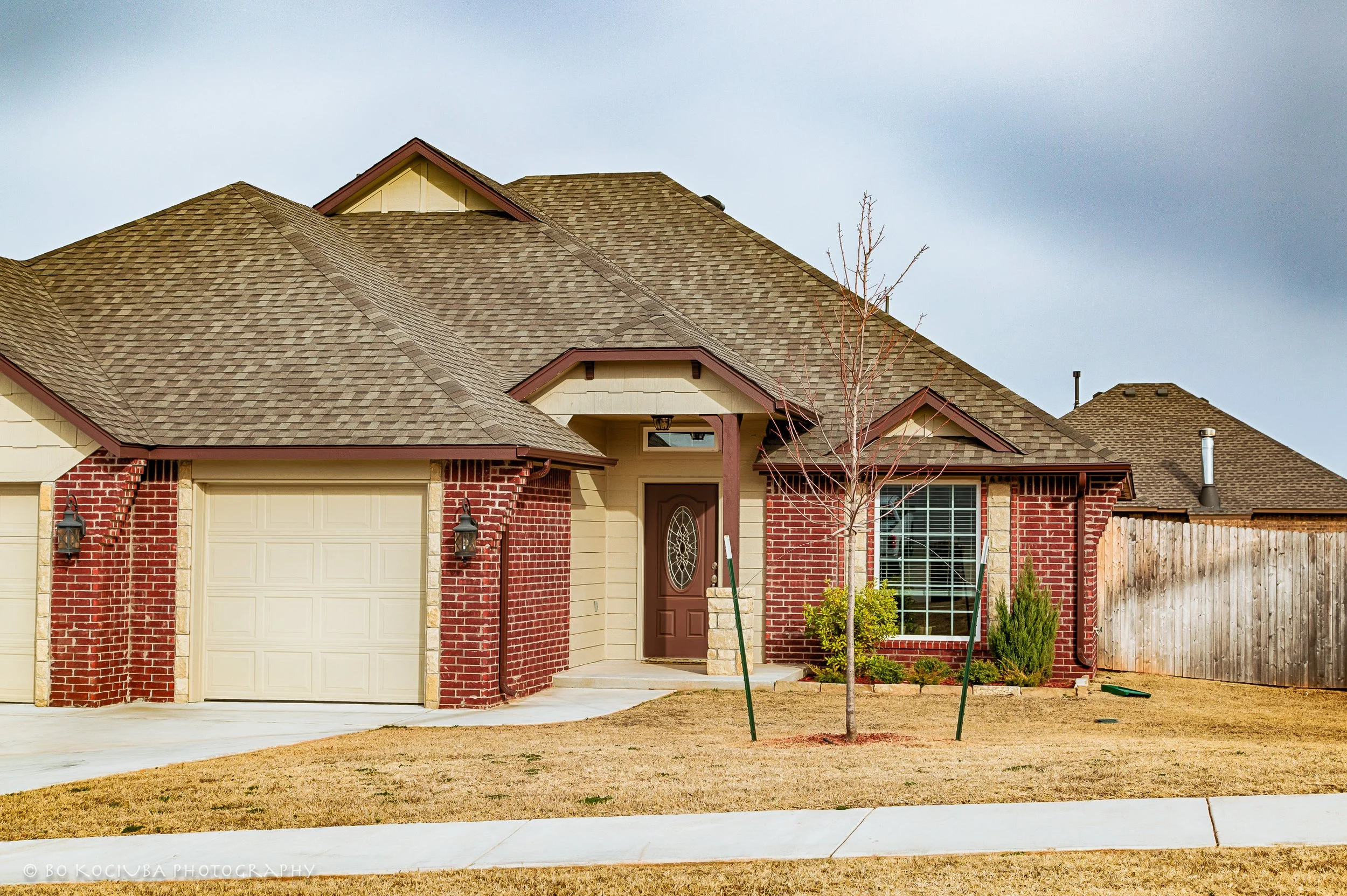 Brick and beige siding home in Chisholm Crossing, Yukon, Oklahoma, featuring a front door with decorative oval glass, attached garage, and landscaped yard.