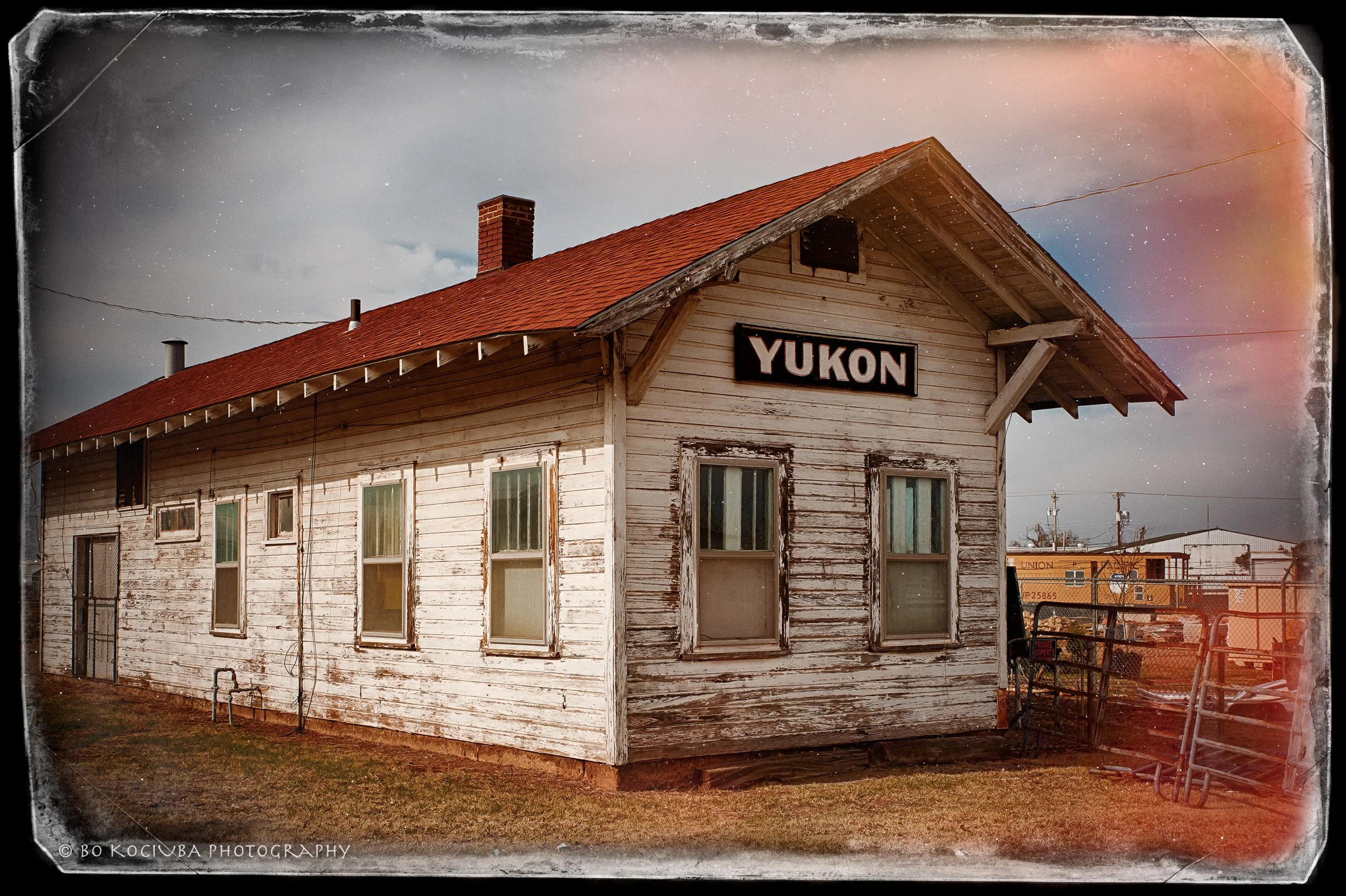 An old, weathered wooden building with a red roof and a smokestack, with a sign labeled "YUKON" on the front, under a cloudy sky with stars visible.