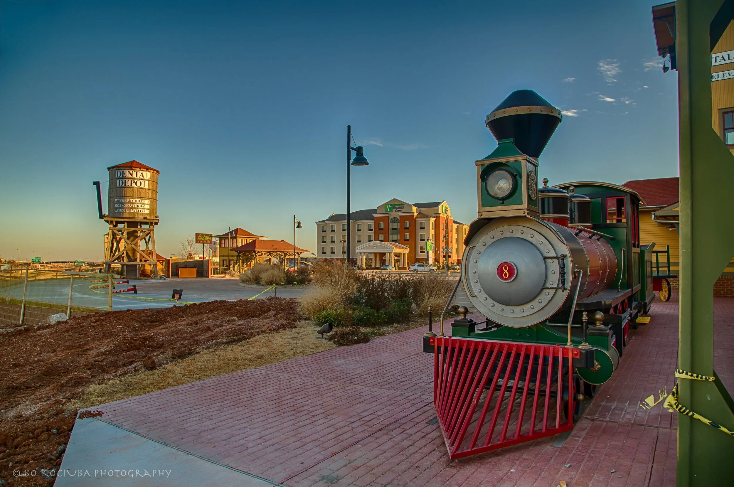 Colorful miniature locomotive outside Dental Depot on Garth Brooks Boulevard in Yukon, Oklahoma, with the building's railroad-themed architecture and water tower.