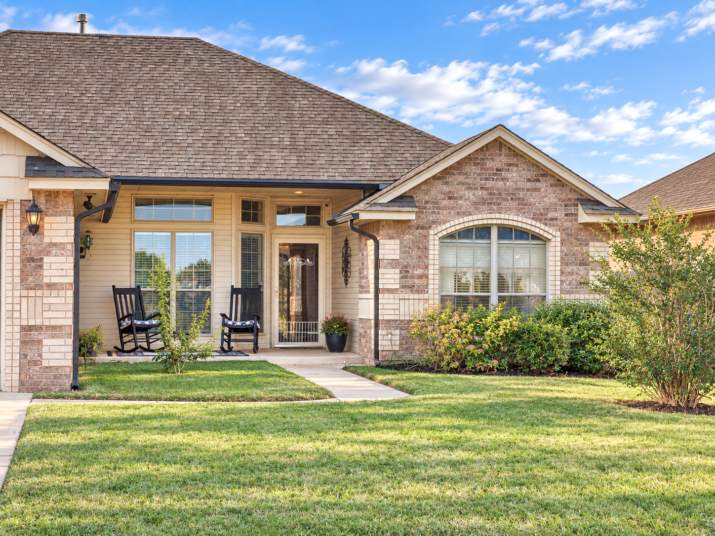 Home Exterior - brick home with a landscaped front yard, covered entry, and black rocking chairs on the porch.