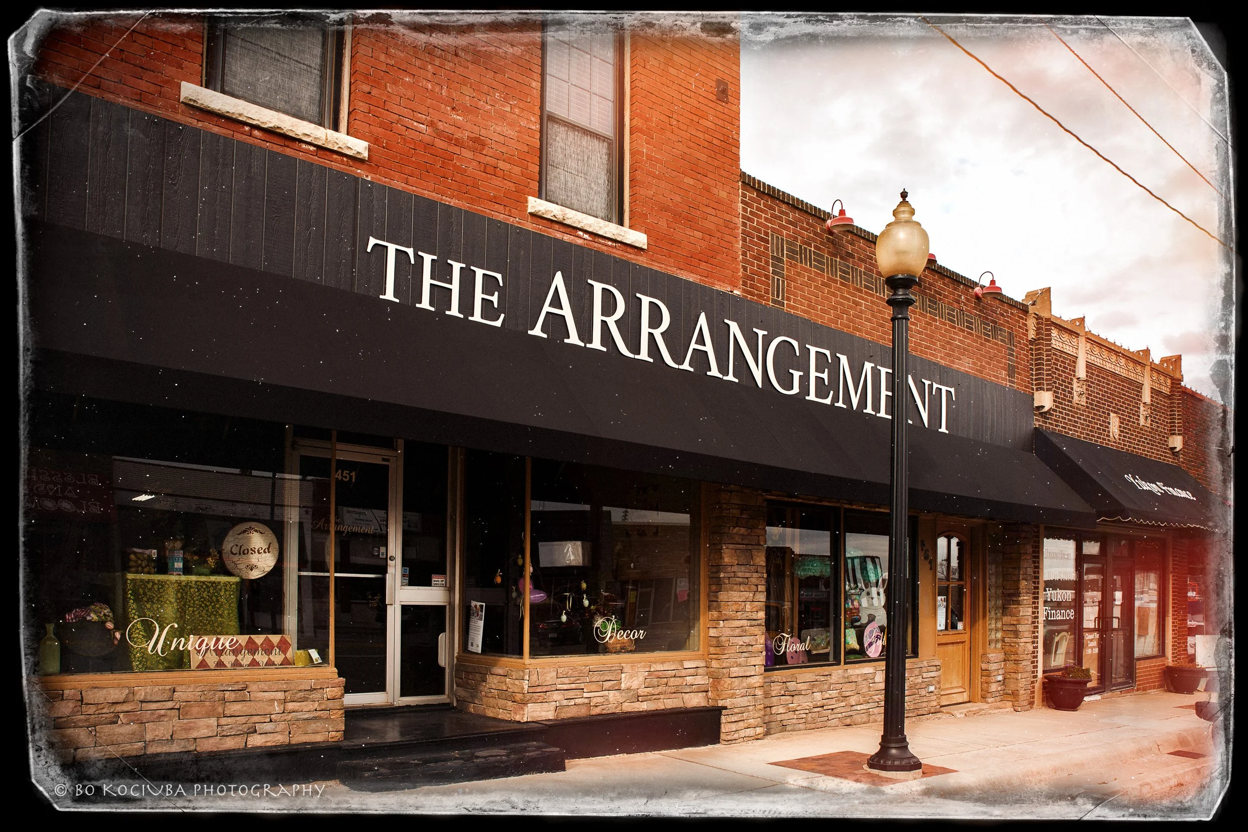 The Arrangement storefront on Main St in Yukon OK with a brick facade, black awning, and window displays featuring home decor and floral arrangements 