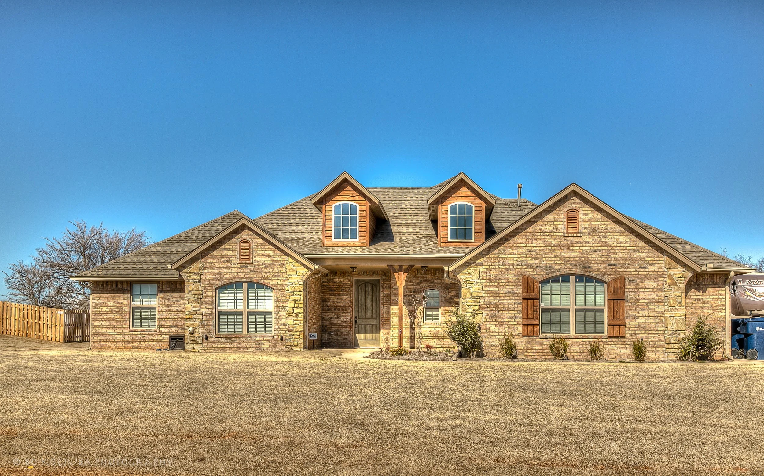 Brick home in Chisholm Run, Yukon, Oklahoma, featuring three dormer windows, wooden shutters, multiple gables, and a spacious front lawn.