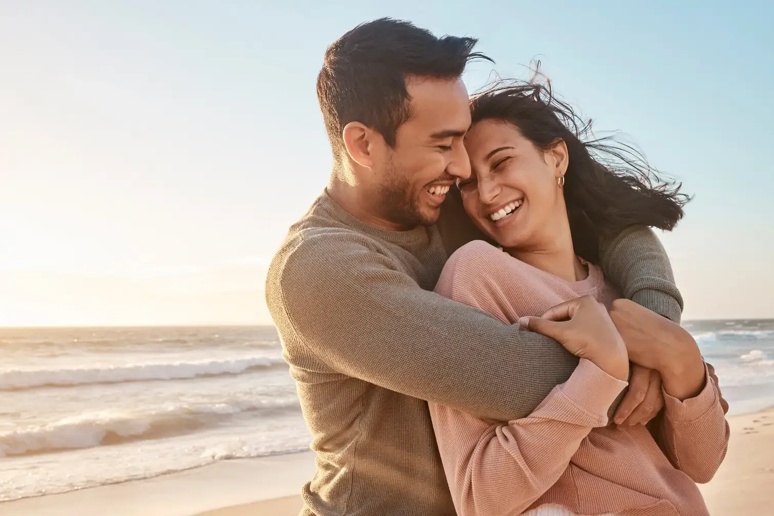 A happy couple hugging on the beach during sunset, smiling and enjoying each other's company.