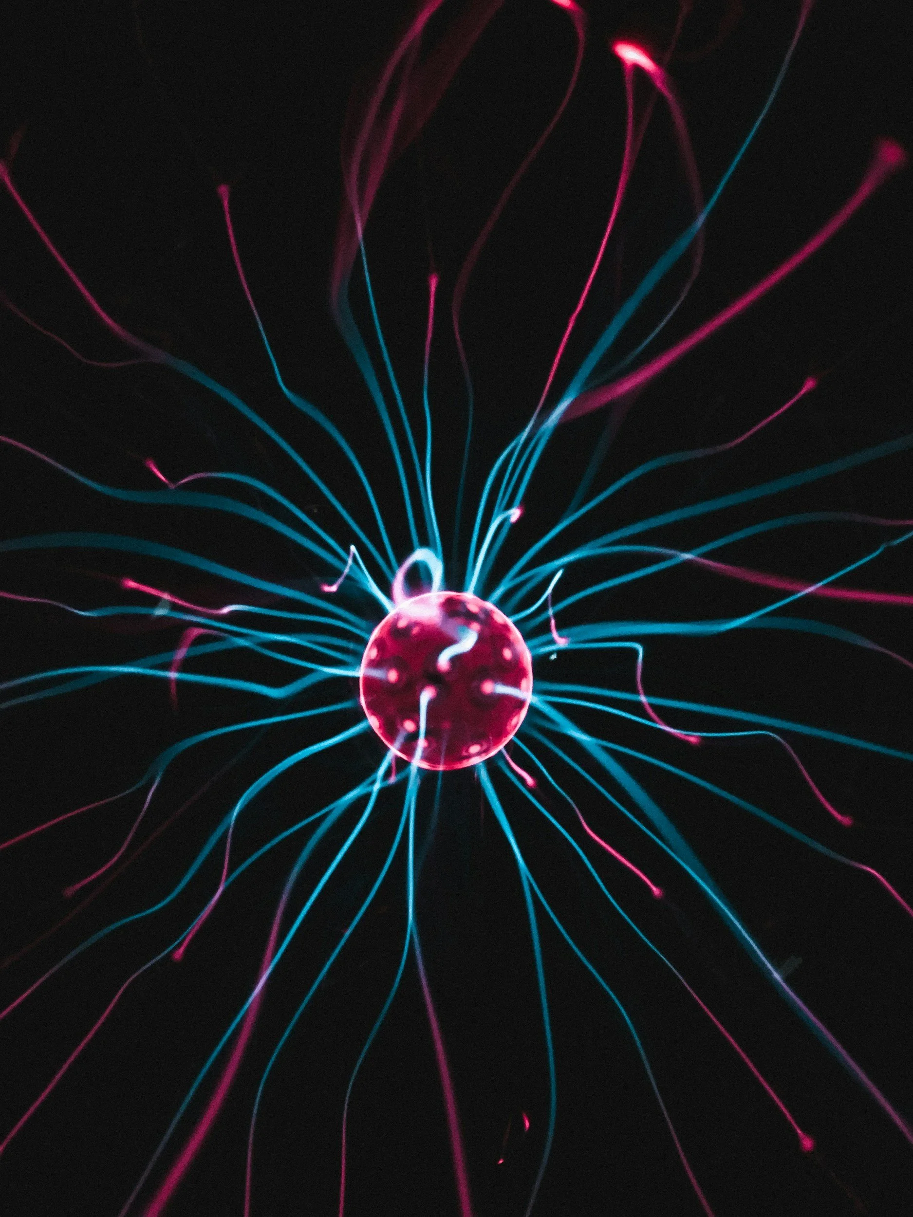 Close-up of plasma ball with colorful electric tendrils emanating from a glass sphere against a black background.