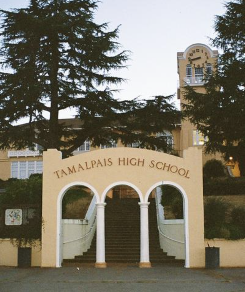 Entrance to Tamalpais High School with stairs, columns, and a clock tower in the background against an early evening sky.