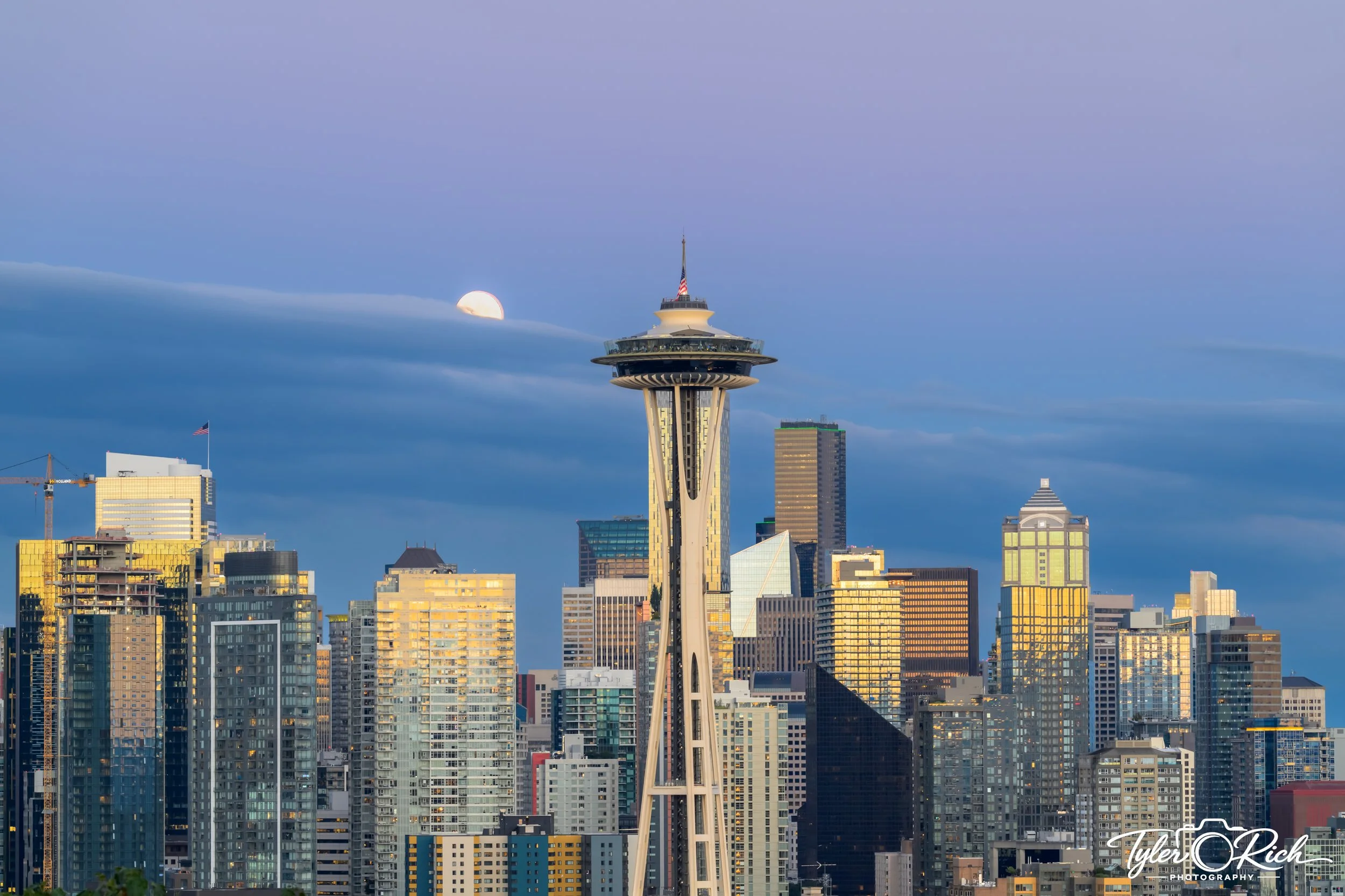 Seattle skyline with the Space Needle in the center, partly cloudy sky with a visible moon at dawn or dusk, surrounded by various tall buildings and skyscrapers.