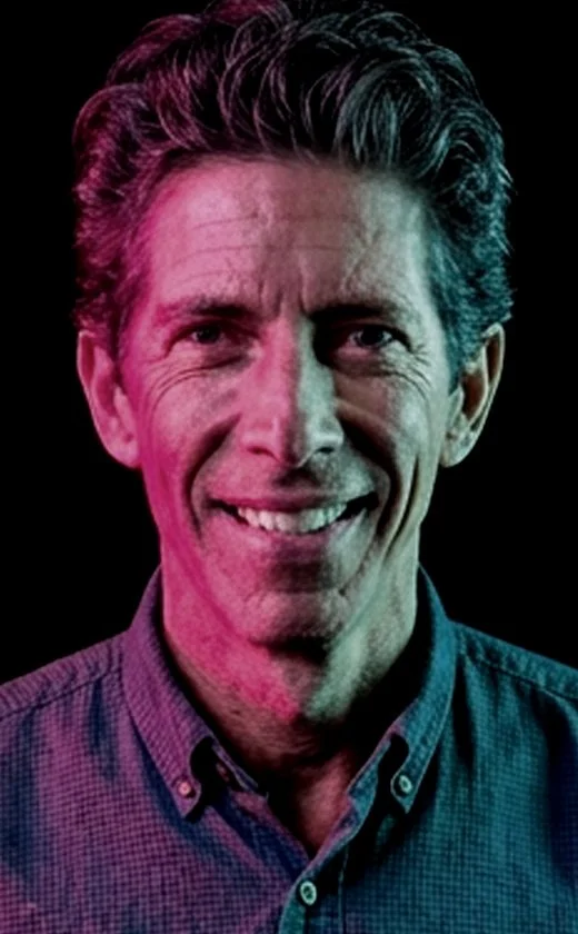 Portrait of a smiling middle-aged man with dark hair, wearing a collared shirt, against a dark background with pink and blue lighting effects.