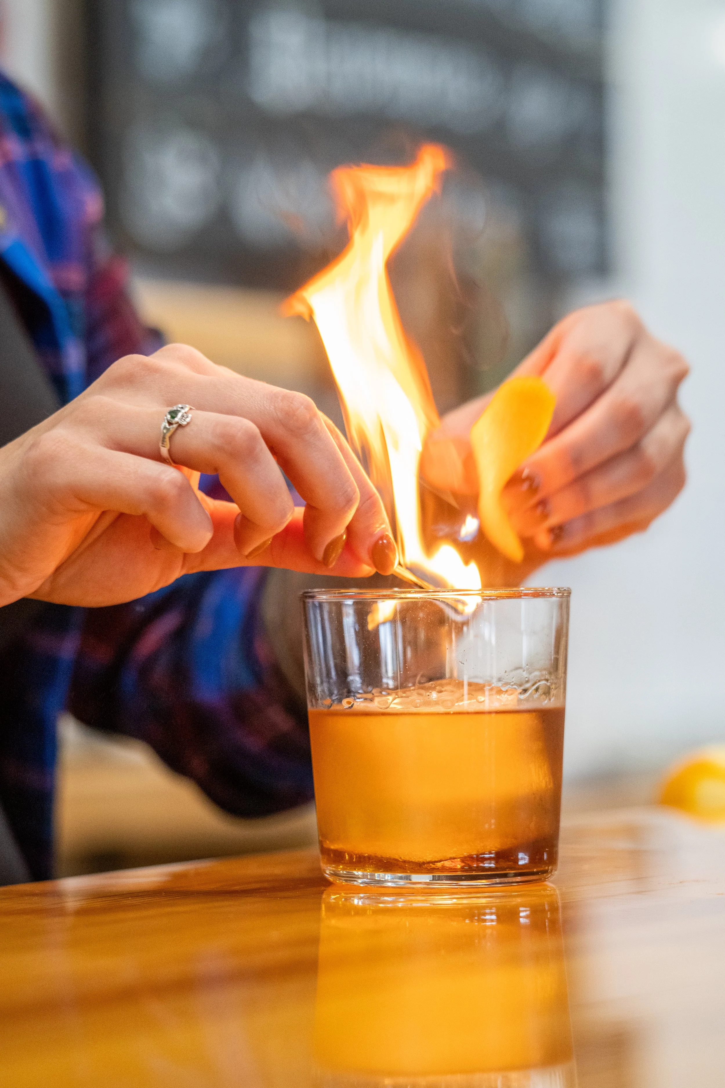 Person holding a yellow item over a glass of orange drink with a flame on top.