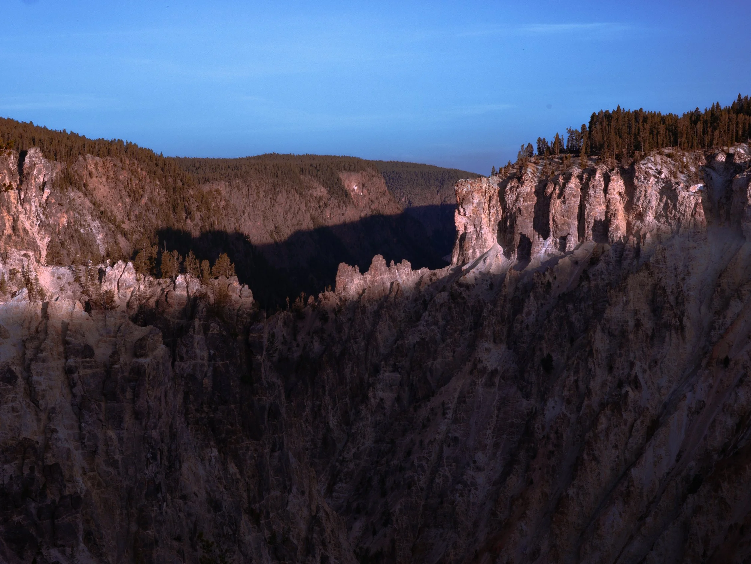 A scenic view of a canyon with rocky cliffs and a forested area on both sides, under a clear blue sky.