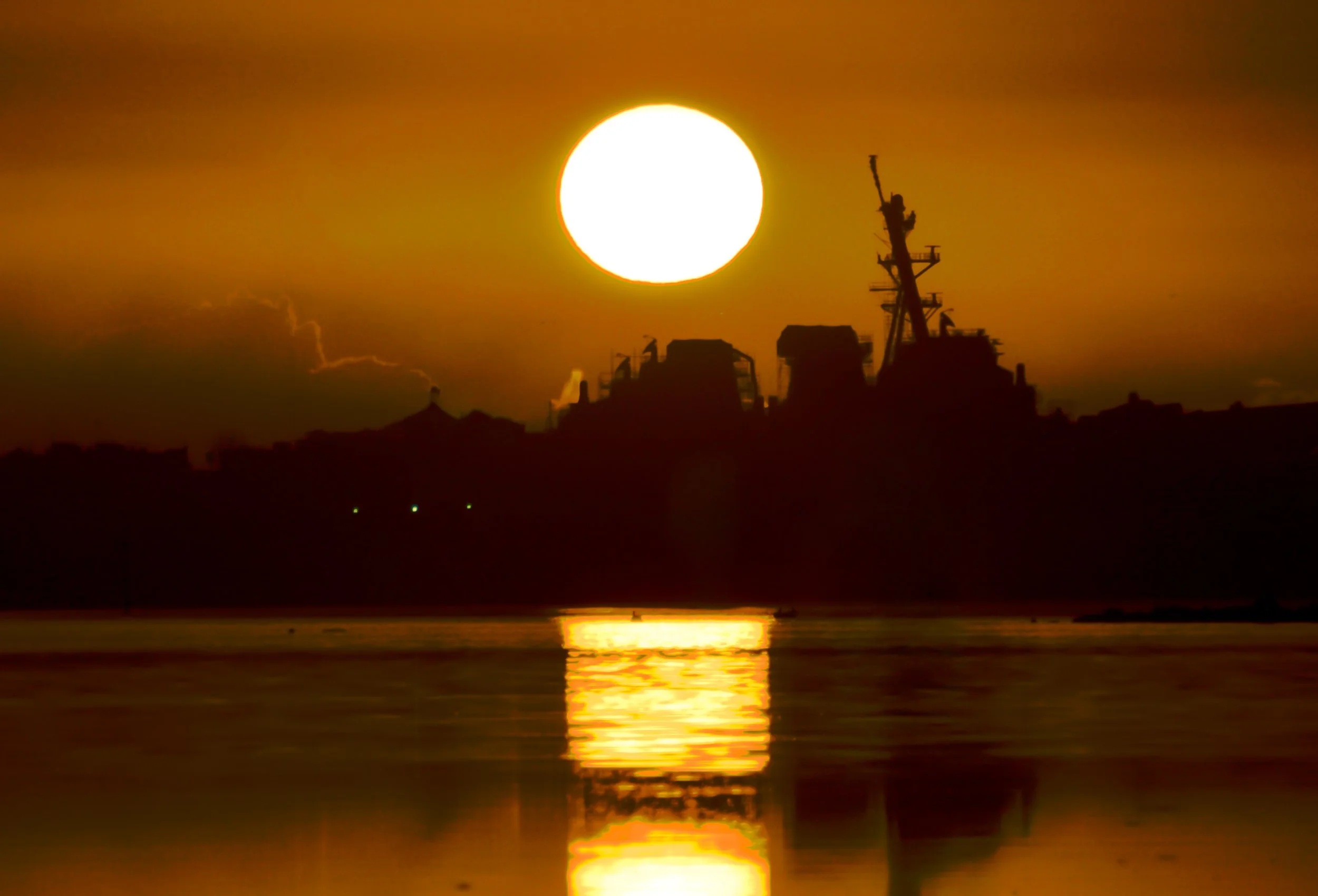 Sunset over the ocean with silhouetted ships on the horizon and reflections in the water.