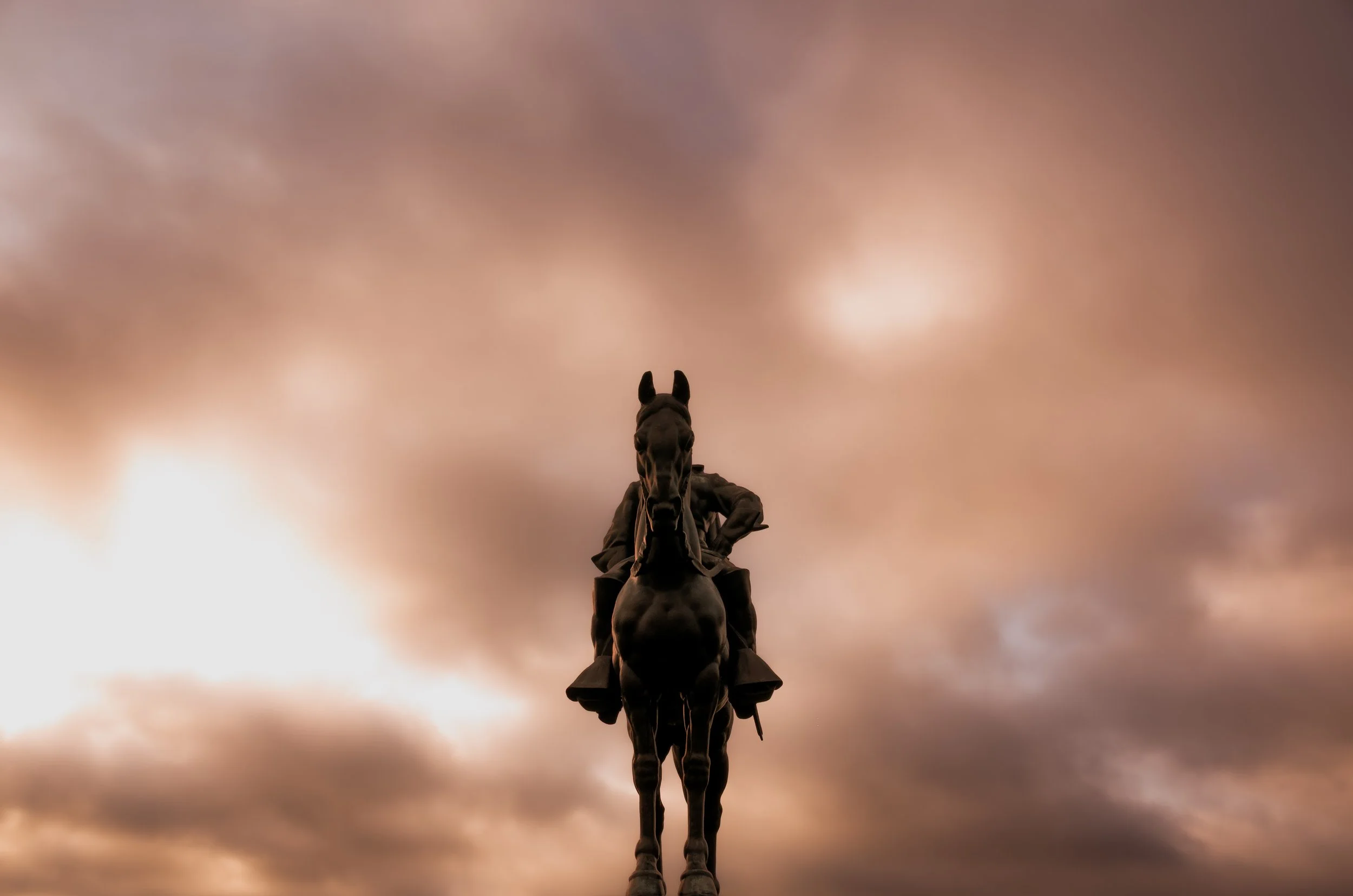 Bronze statue of a man on horseback viewed from below, with a cloudy sky in the background.