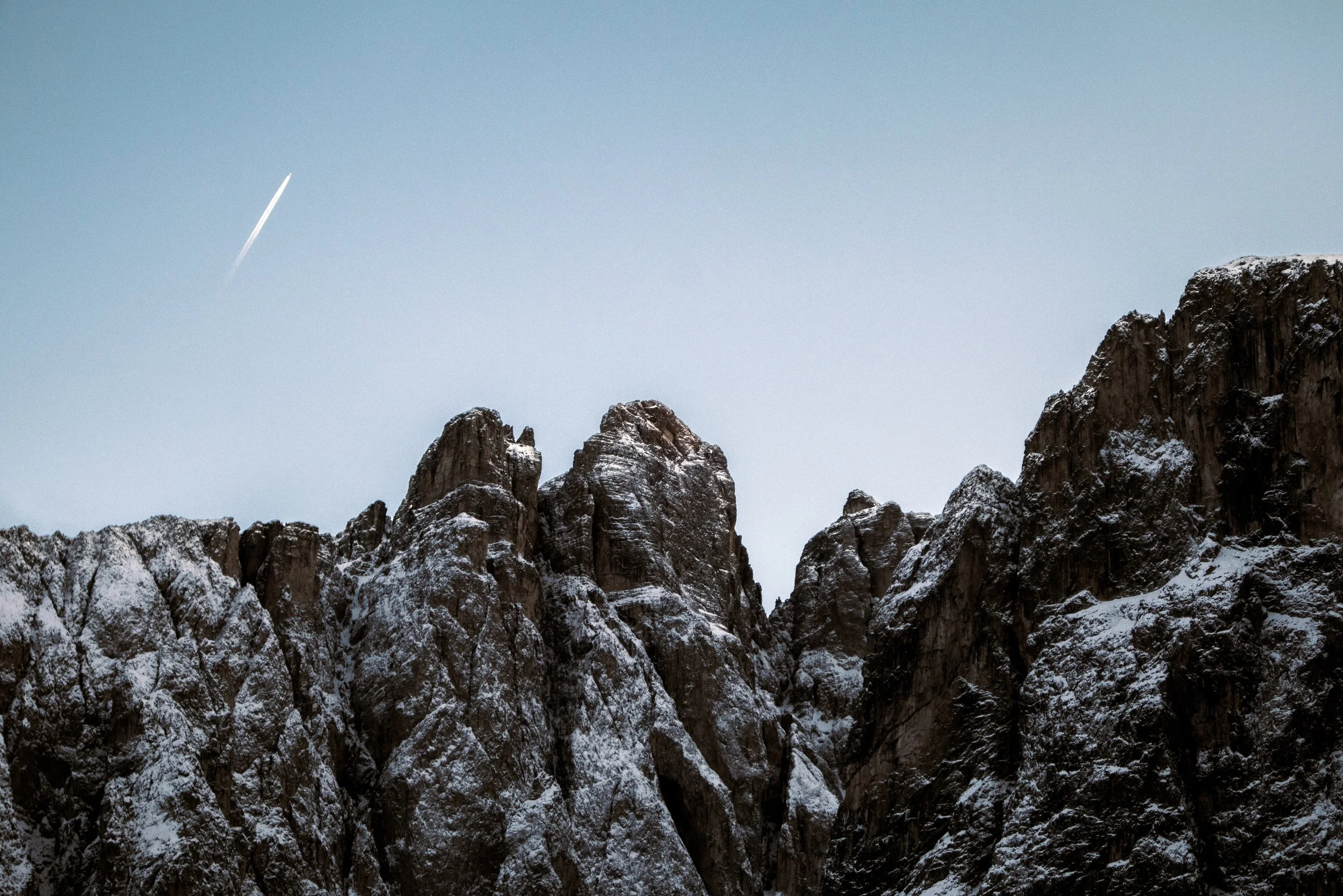 Snow-covered mountain peaks under a thin, clear sky with a small contrail visible.