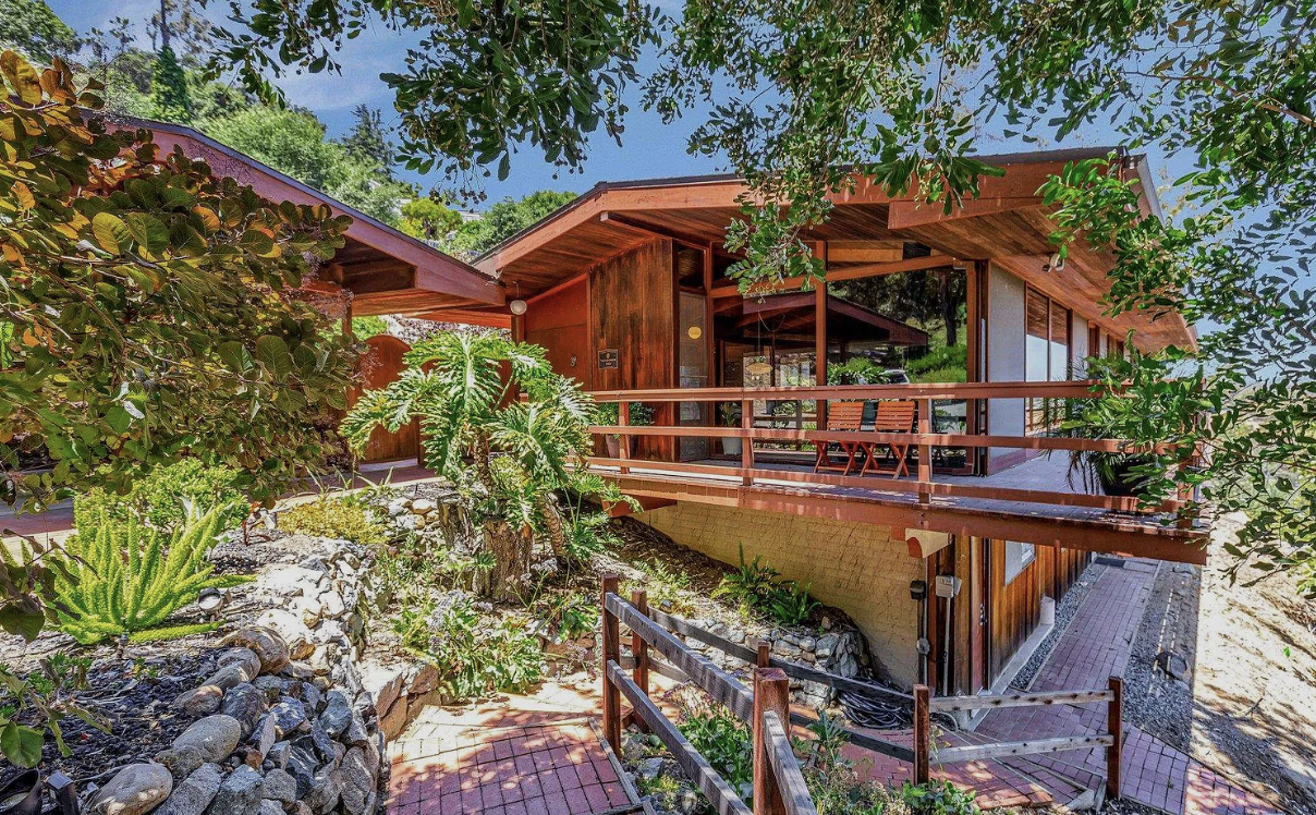 A Lloyd Ruocco house in San Diego, with redwood walls and low pitched roofs over a wide deck on a planted hillside, and brick paths below.