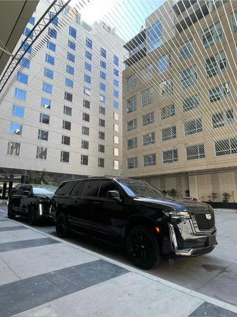 Black SUV parked outside between two tall buildings with reflective windows in an urban area.