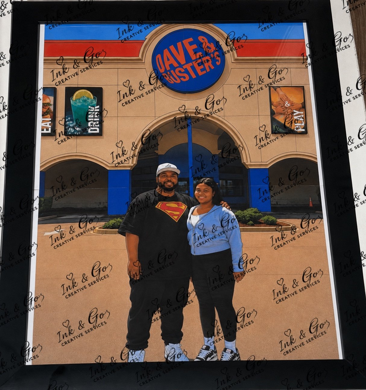 Two people smiling and standing together in front of a Dave & Buster's storefront sign. The person on the left is wearing a Superman shirt and baseball cap, and the person on the right is wearing a blue hoodie. The storefront has images of a drink and a hand holding a game controller.