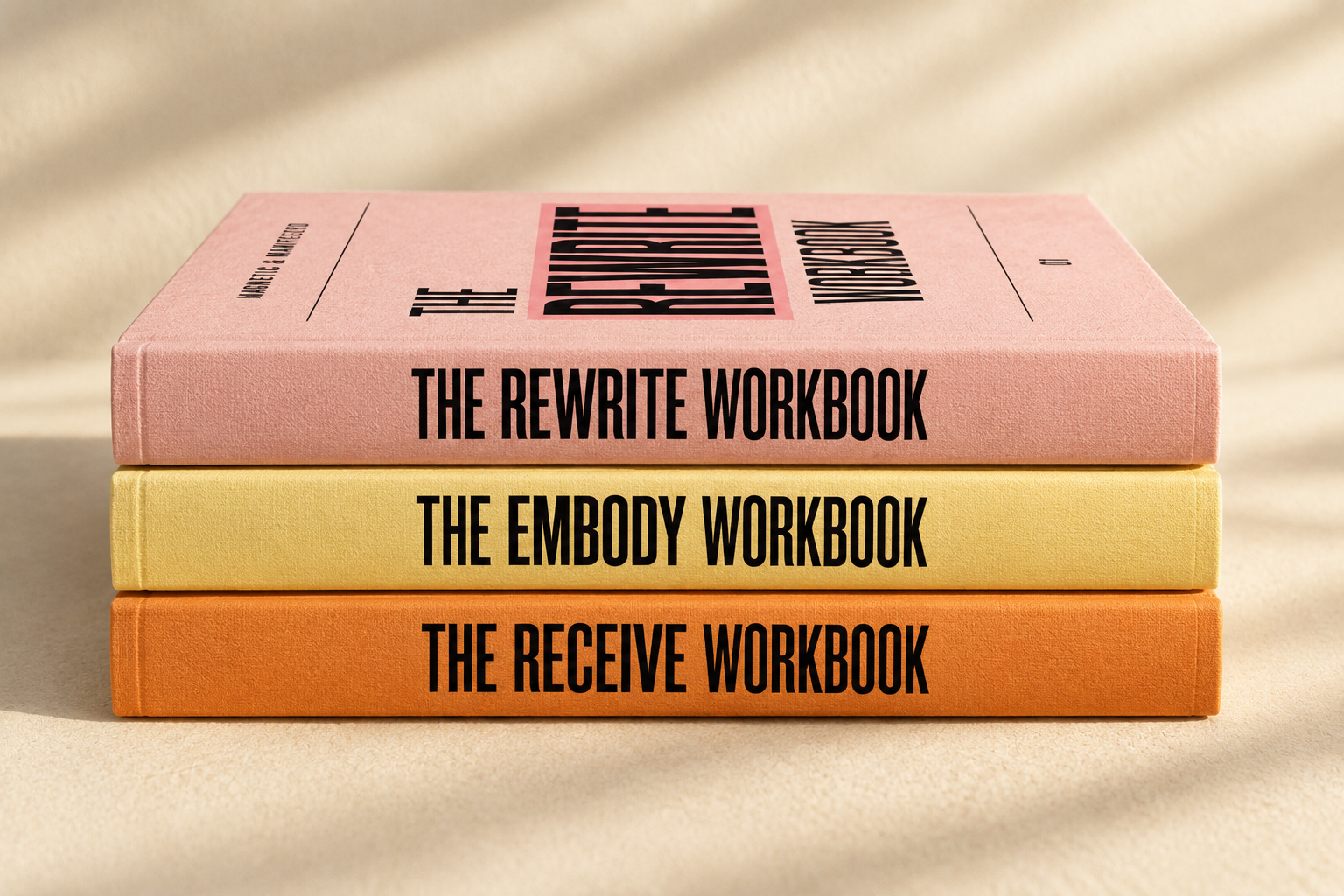 Stack of three books titled 'The Rewrite Workbook,' 'The Embody Workbook,' and 'The Receive Workbook,' with pastel-colored covers in pink, yellow, and orange, placed on a beige surface.