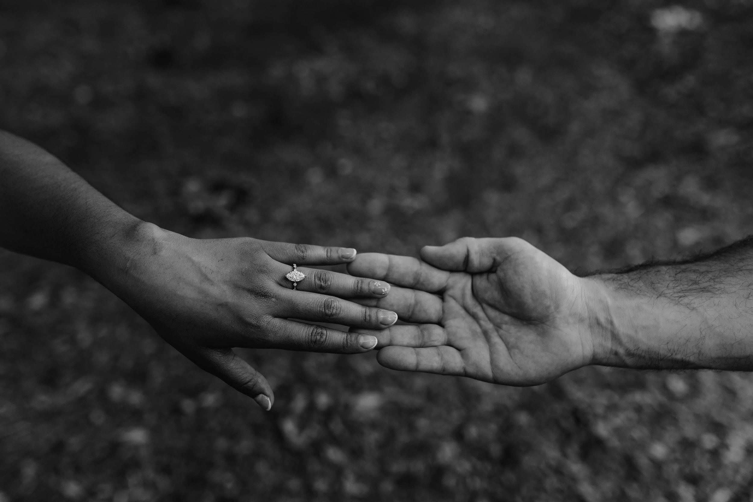 Two hands, one with a ring, holding each other against a blurred background.