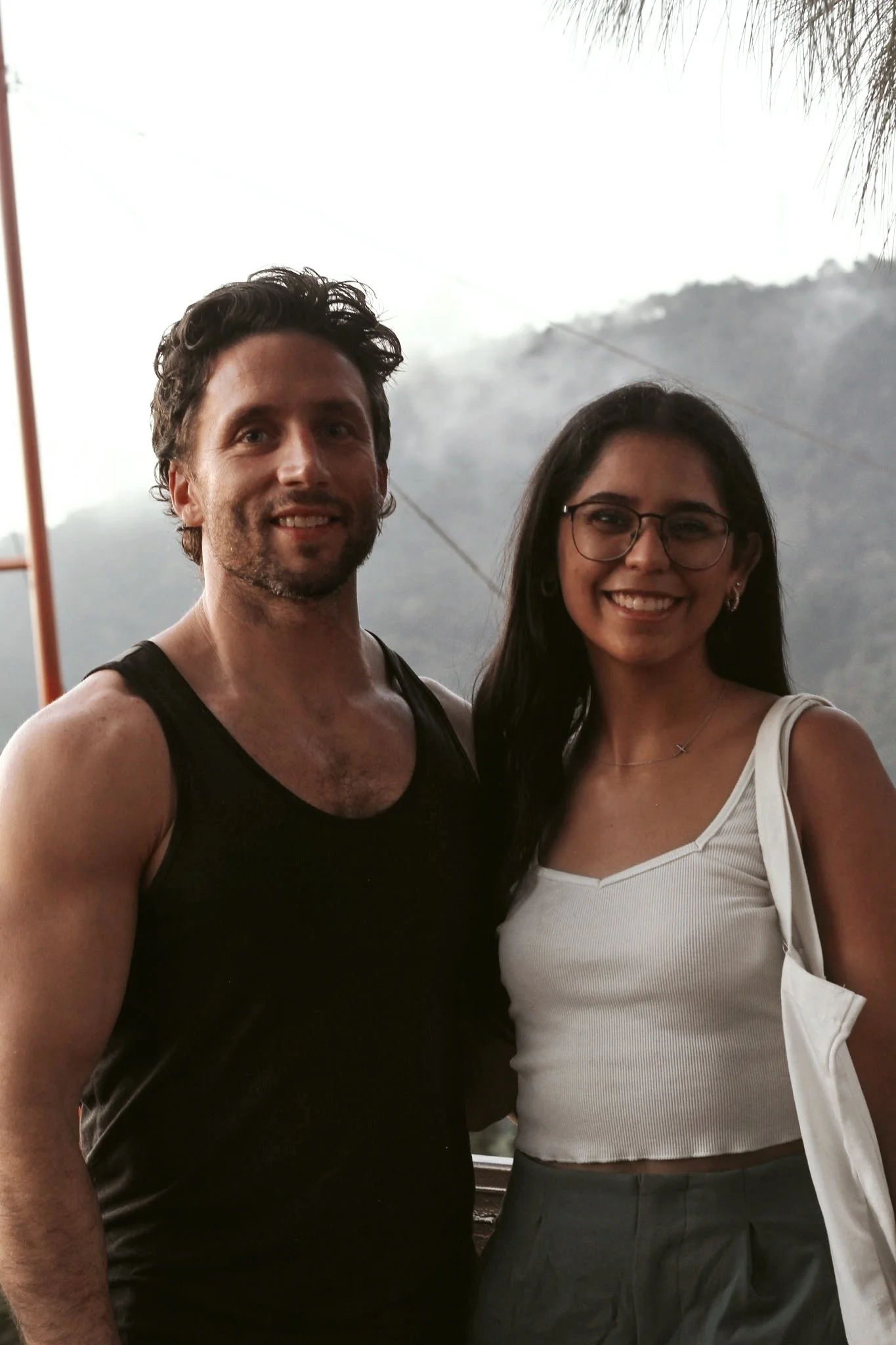 Two people standing close together outdoors against a mountain background, smiling for the camera.