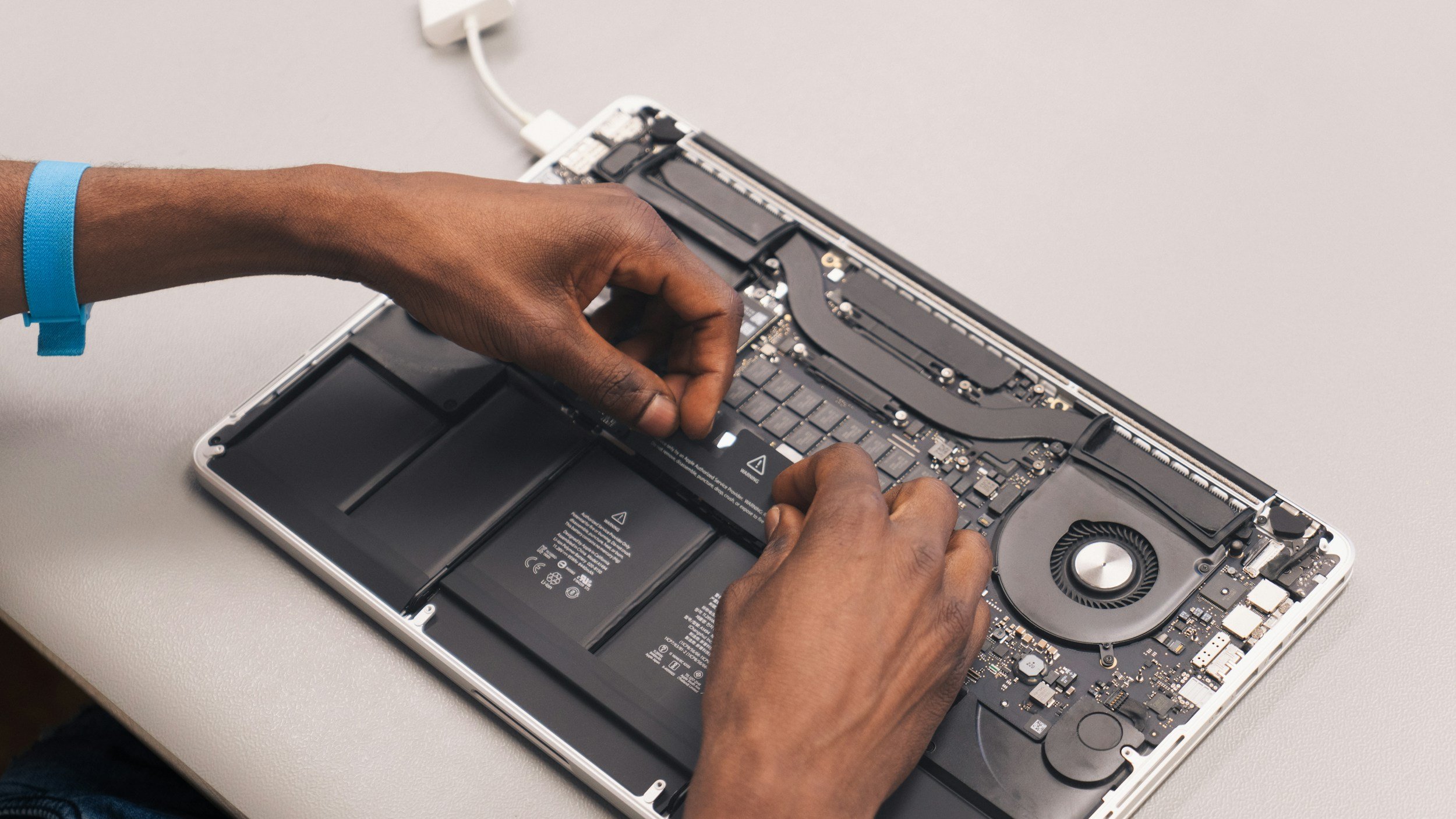 Technician's hands servicing the internal components of an open laptop