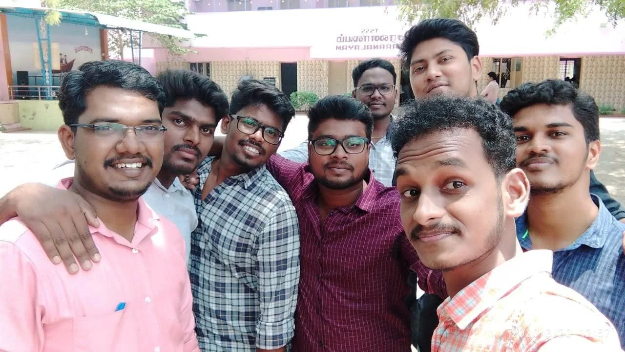 Group of nine young men taking a selfie outdoors, smiling at the camera.