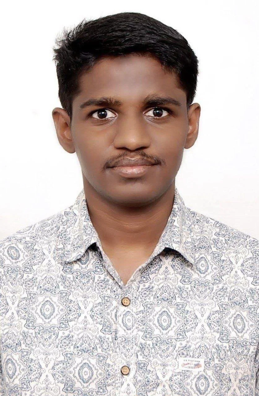 A young man with short black hair and brown skin, wearing a light patterned shirt against a white background.